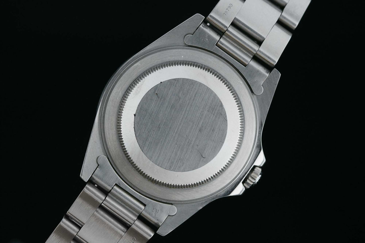 A close-up of the Rolex Explorer II by Rolex, highlighting its stainless steel bracelet, brushed and plain case back, and notched edges typical of this iconic sport watch.