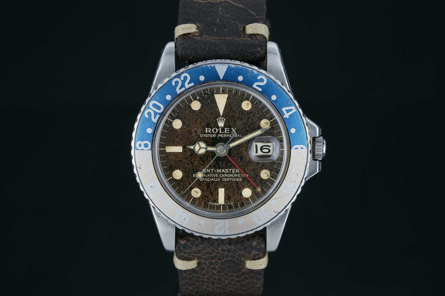 A vintage Rolex GMT-Master by Rolex featuring a faded blue and silver bezel, brown patina dial, large luminous markers, and a worn brown leather strap, showcased against a black background.