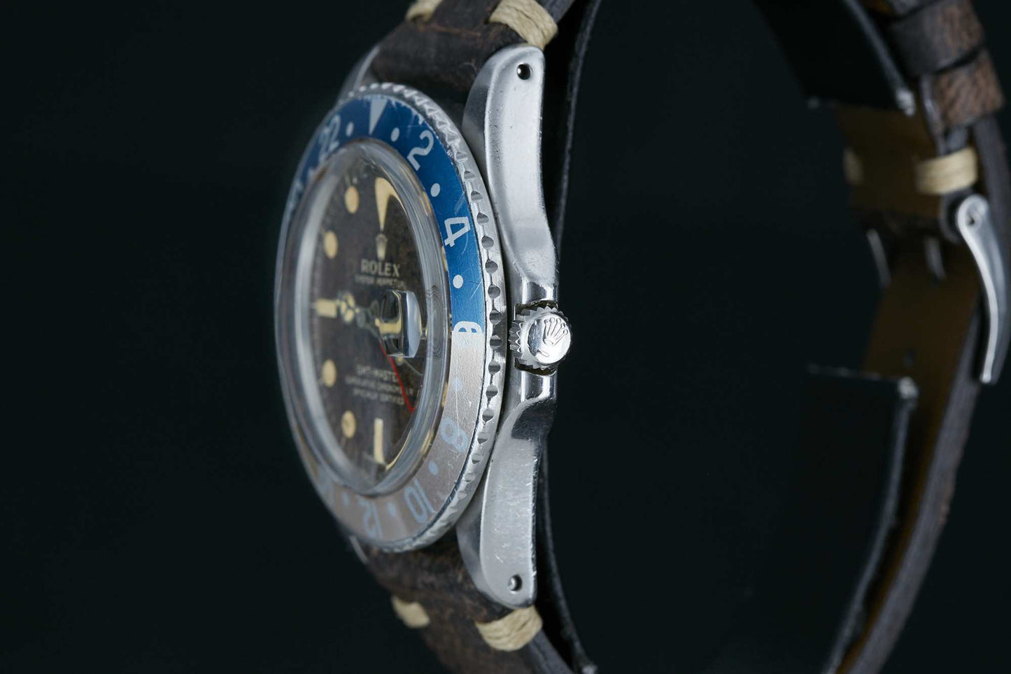 Side view of a vintage Rolex GMT-Master by Rolex, featuring a blue and silver bezel, brown leather strap, worn dial with luminous markers and hands, and visible branded crown—a true classic among sport watches.