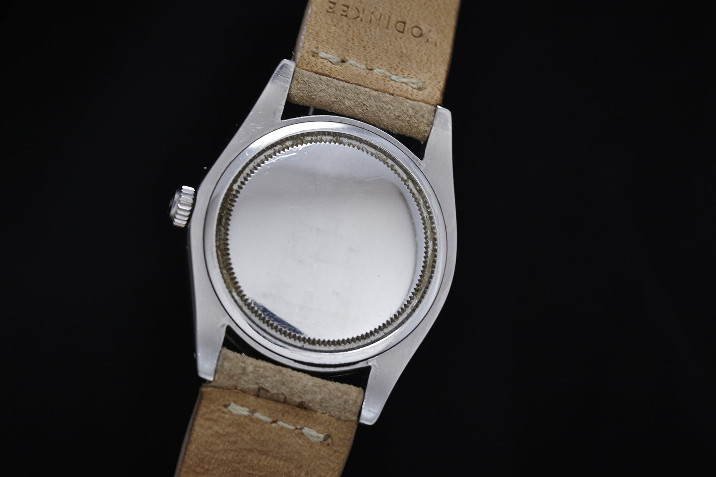 A close-up of the back of a 1978 Rolex Oysterdate Precision with a tan leather strap, set against a black background. The smooth, round case is unmarked, showcasing classic Rolex craftsmanship.