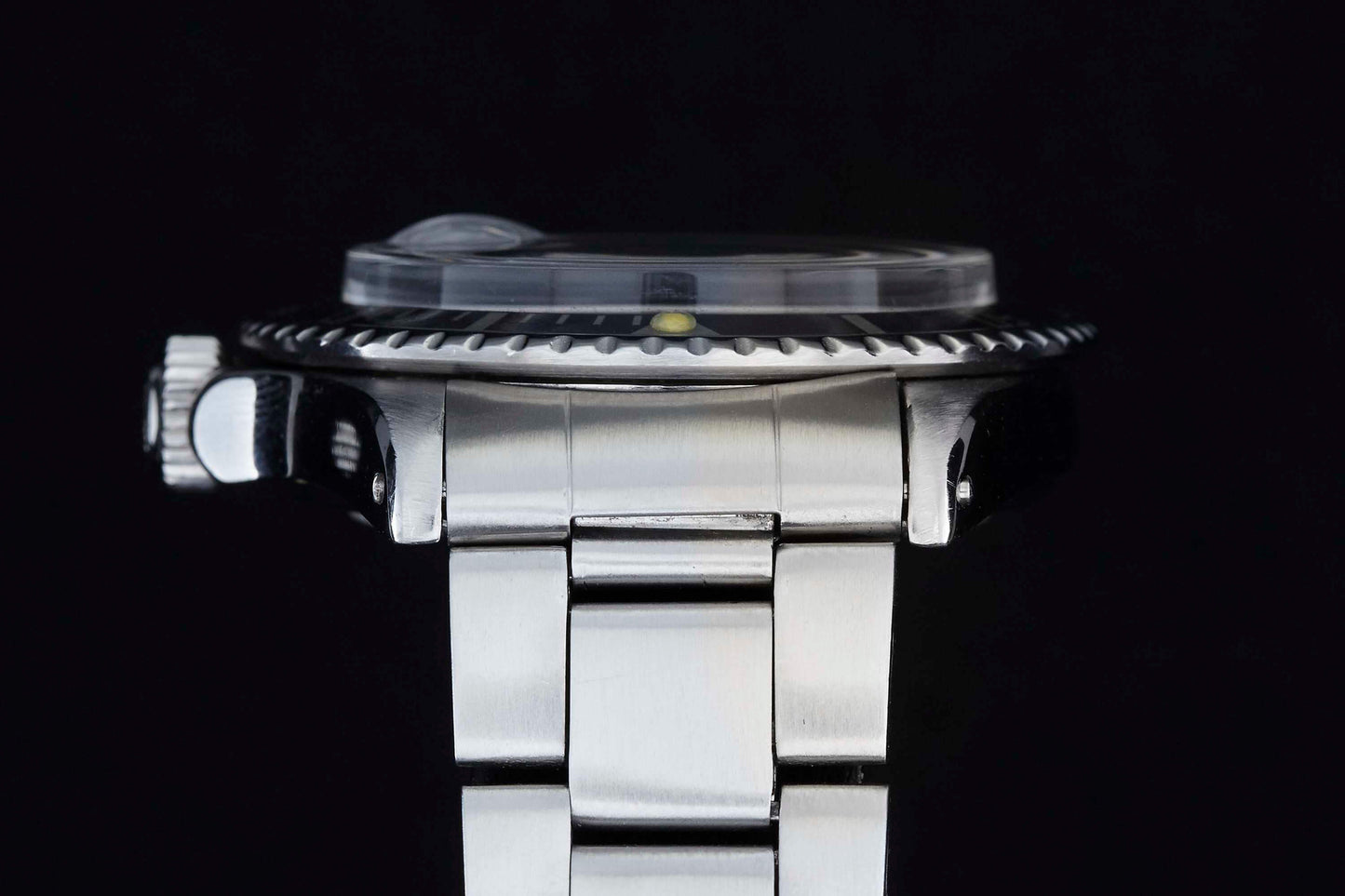 Side view of the Rolex Submariner by Rolex, a silver metal dive watch with ridged bezel, crown, and linked bracelet. The partially visible dial and domed crystal evoke its iconic style against a black background.