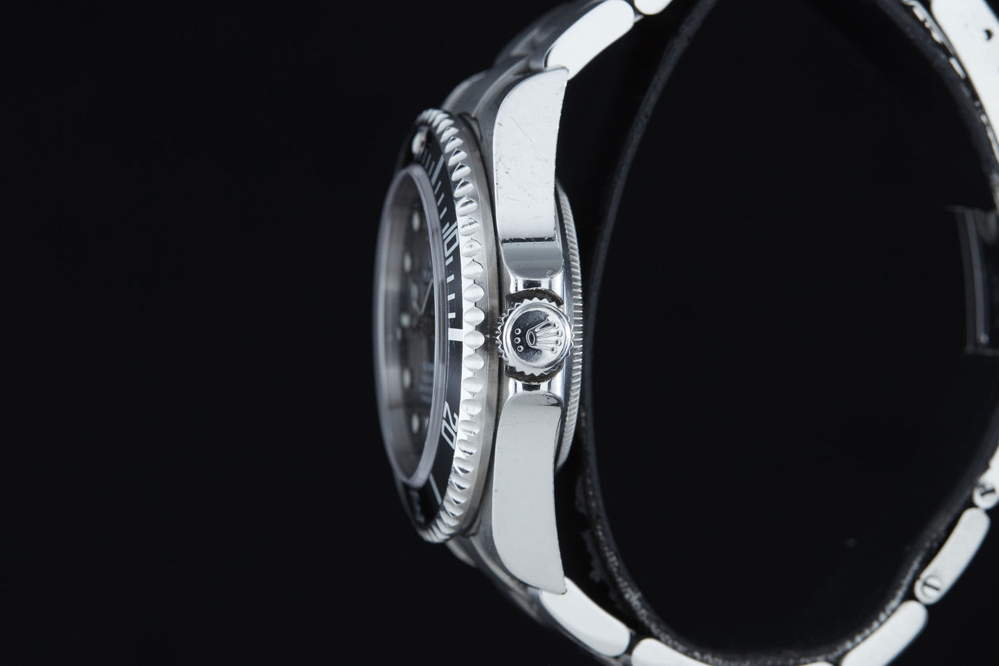 A close-up side view of the Rolex Sea Dweller by Rolex, featuring a silver ridged bezel and a crown with the brand’s logo, set against a black background—a timepiece renowned for its use by COMEX divers in saturation diving.
