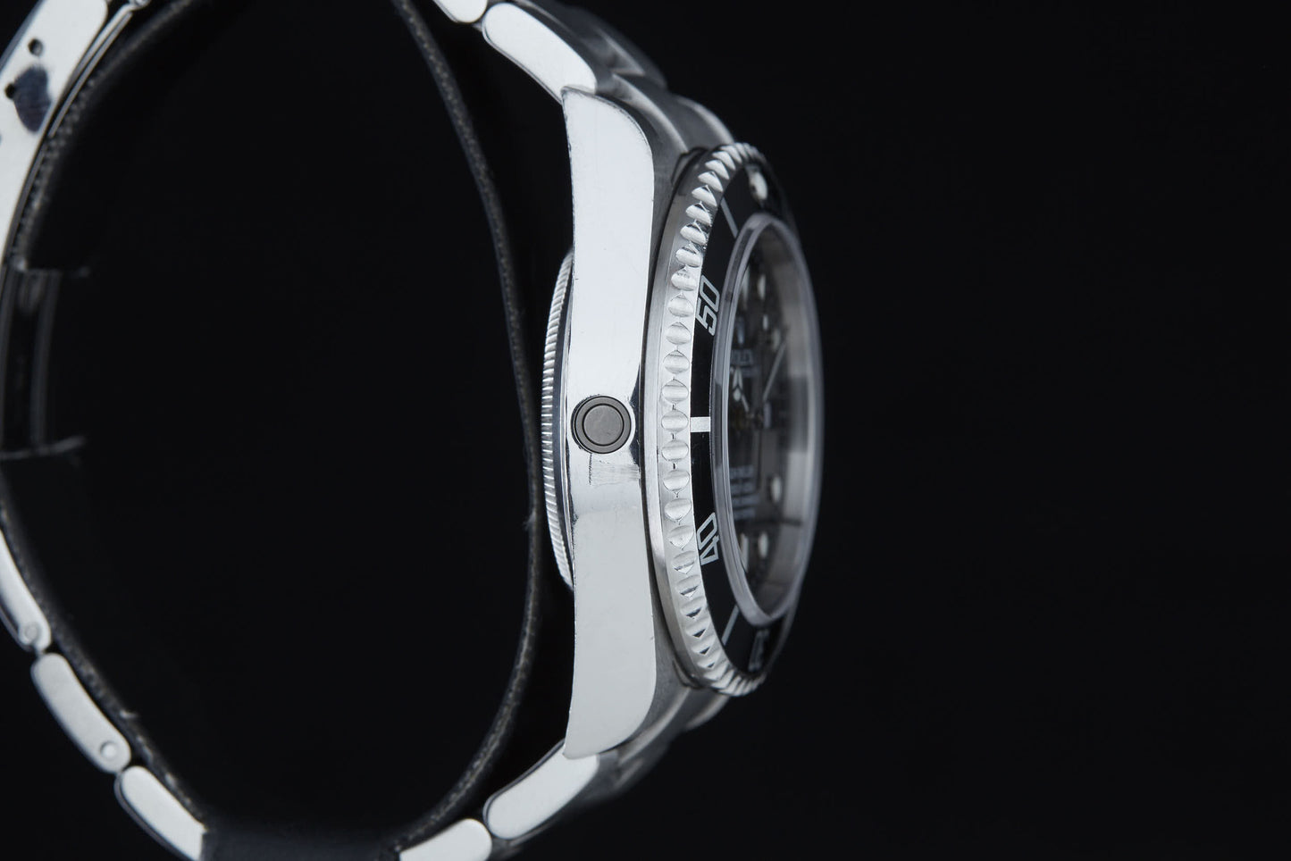 A close-up side view of the Rolex Sea Dweller by Rolex, featuring a silver case and black band, highlights its crown and bezel—engineered for saturation diving with a design echoing COMEX divers—set against a black background.