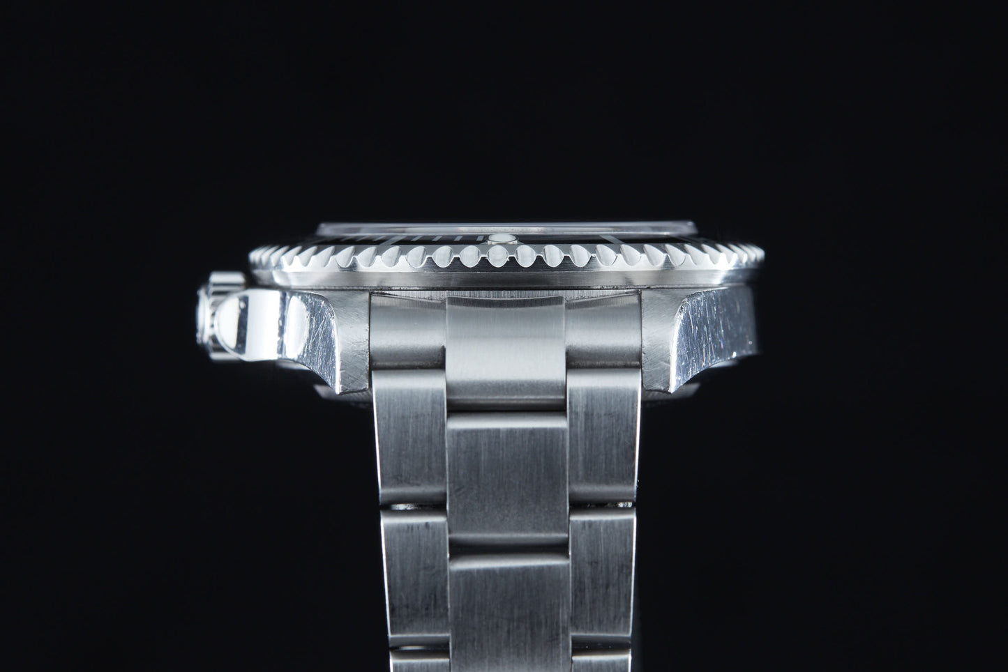 A close-up side view of the Rolex Sea Dweller by Rolex shows its stainless steel bracelet, crown, and grooved bezel—designed for saturation diving—set against a black background.