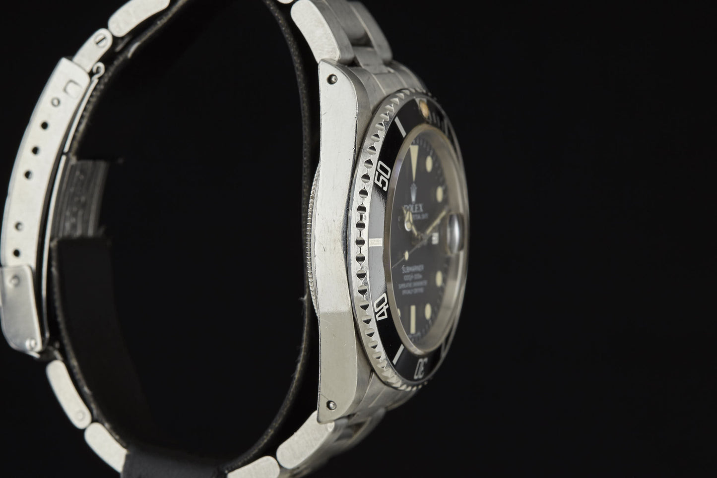 Close-up side view of the Rolex Submariner by Rolex, showcasing its black band, visible bezel, and luminous hour markers on a dark dial—all set against a black background for a look of classic elegance.