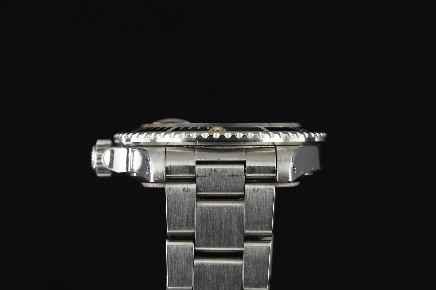 A close-up side view of the Rolex Submariner luxury watch by Rolex, featuring a stainless steel band and ridged bezel, set against a plain black background.