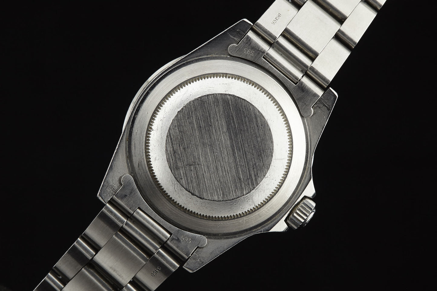 The image shows the back of a Rolex Submariner by Rolex, featuring a brushed stainless steel finish, metal link band, and a round case back reminiscent of classic vintage designs.