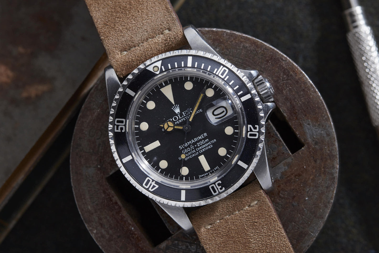 A Rolex Submariner dive watch by Rolex, featuring a brown leather strap, black dial with white markers, and date display, rests on a round metal object.