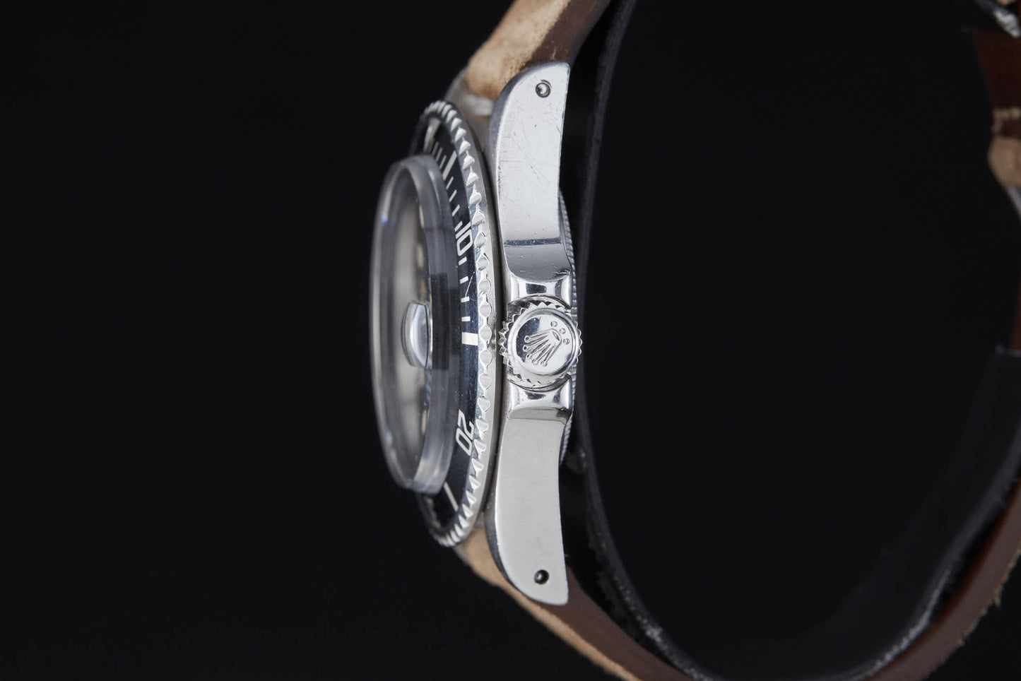 Side view of the Rolex Submariner by Rolex, featuring a silver case, brown leather strap, textured bezel, and signature crown logo—set against a black background.