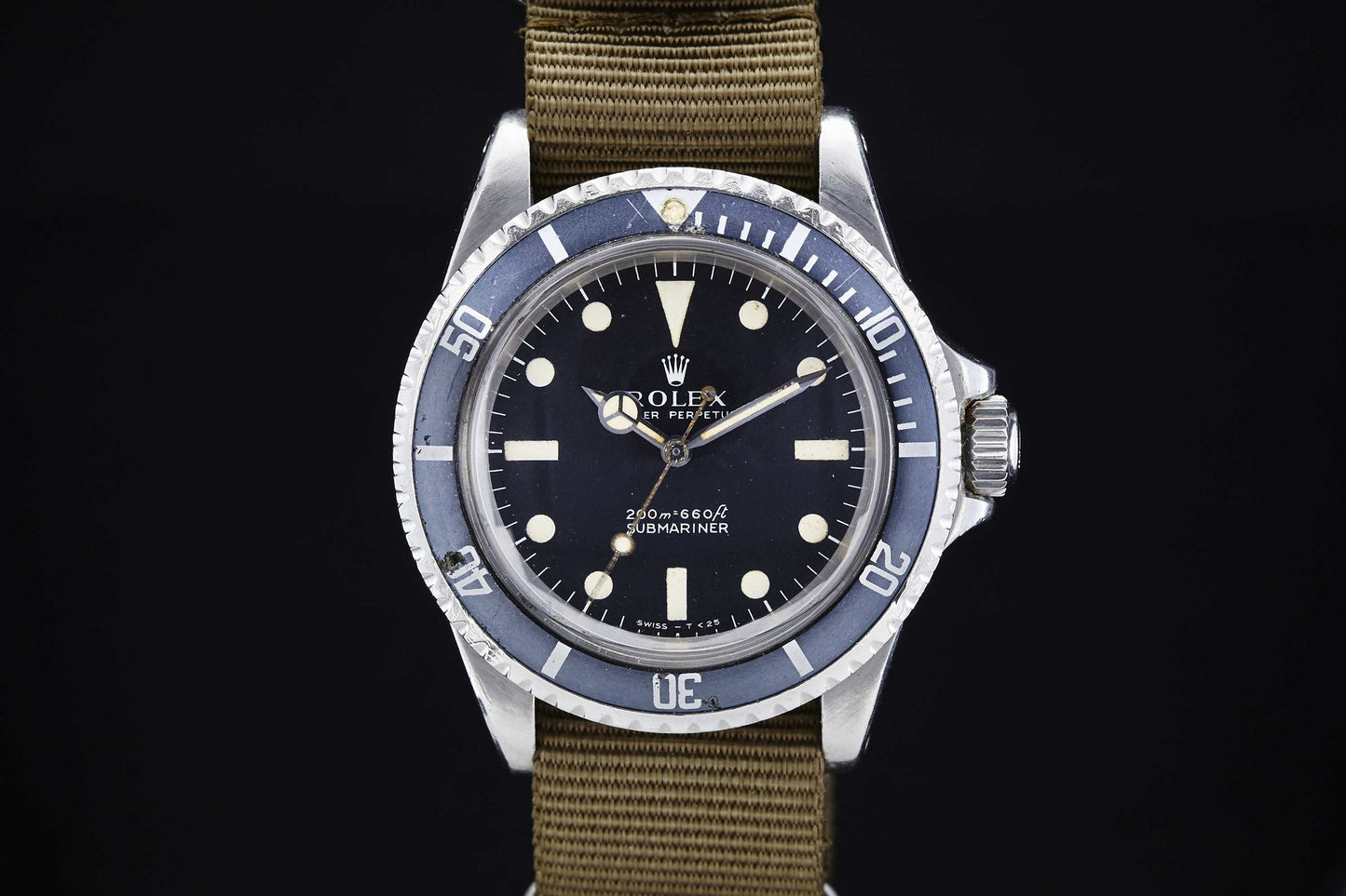 The Rolex Submariner, a vintage tool watch by Rolex with a black dial, white hour markers, and rotating bezel, is showcased on an olive green NATO strap against a black background.