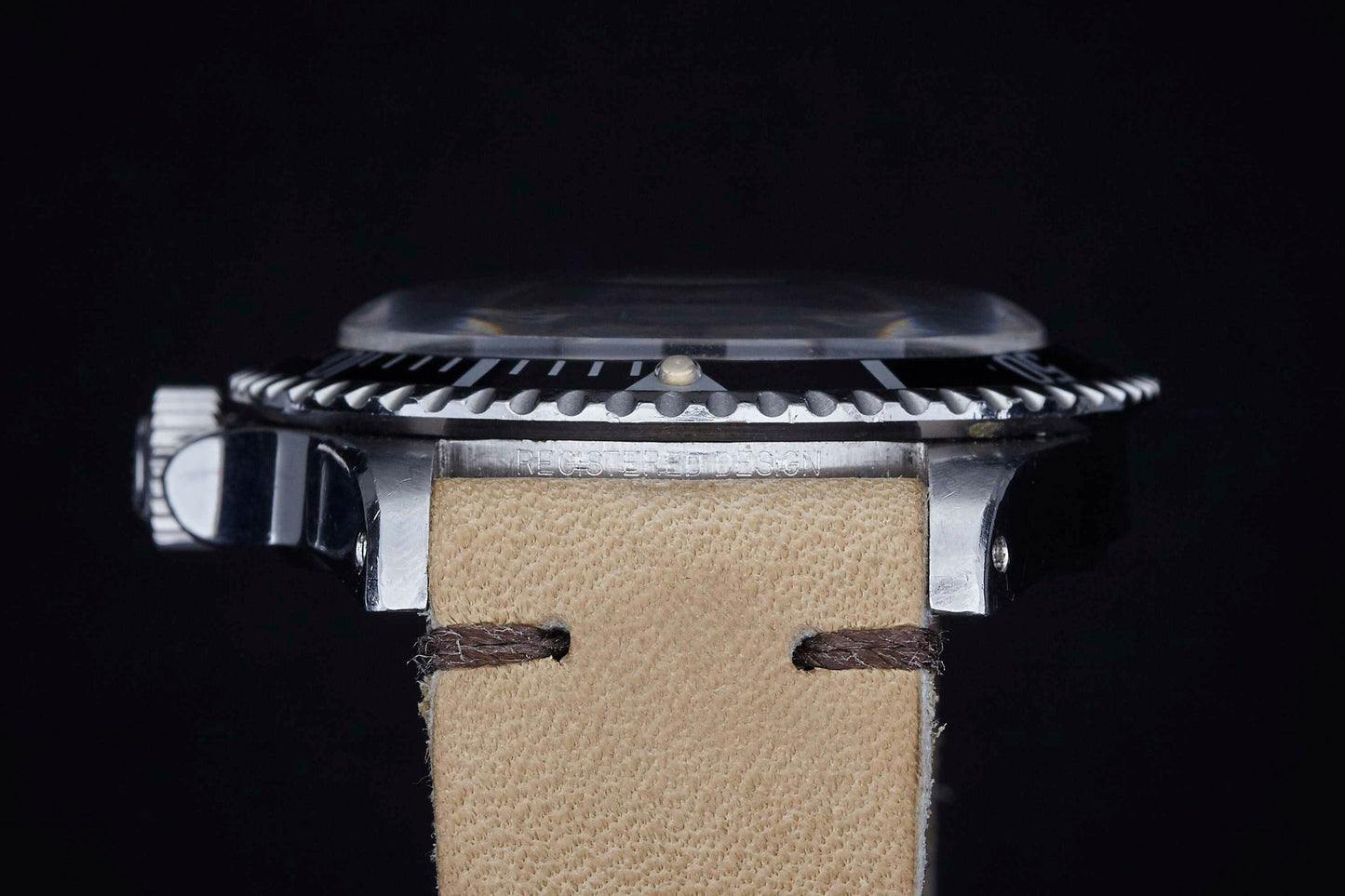 Close-up side view of a Rolex Submariner wristwatch by Rolex, featuring a beige leather strap, black bezel, and prominent silver crown set against a dark background.