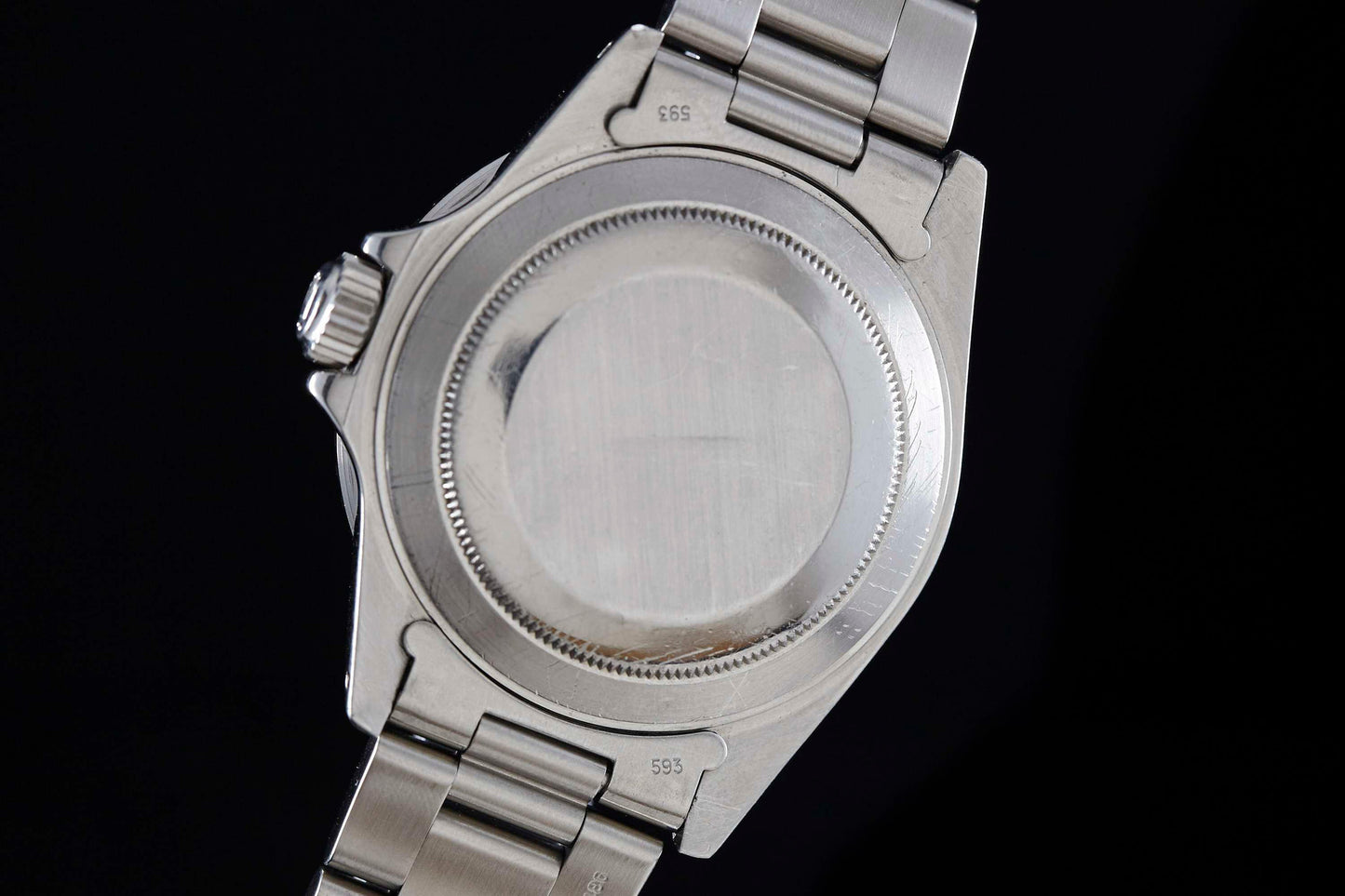 Close-up of the back of a Rolex Submariner Date by Rolex against a black background, highlighting its smooth, round case back and part of the metal bracelet.