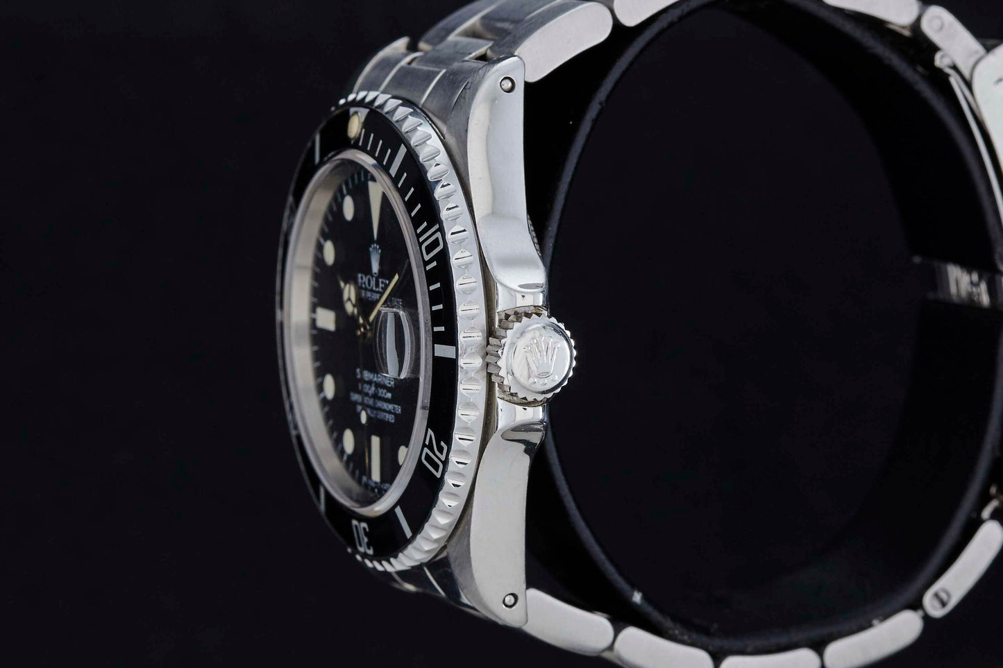 A close-up side view of the Rolex Submariner Date by Rolex, in silver with a black bezel and dial, displays the crown and part of the bracelet against a plain black background.