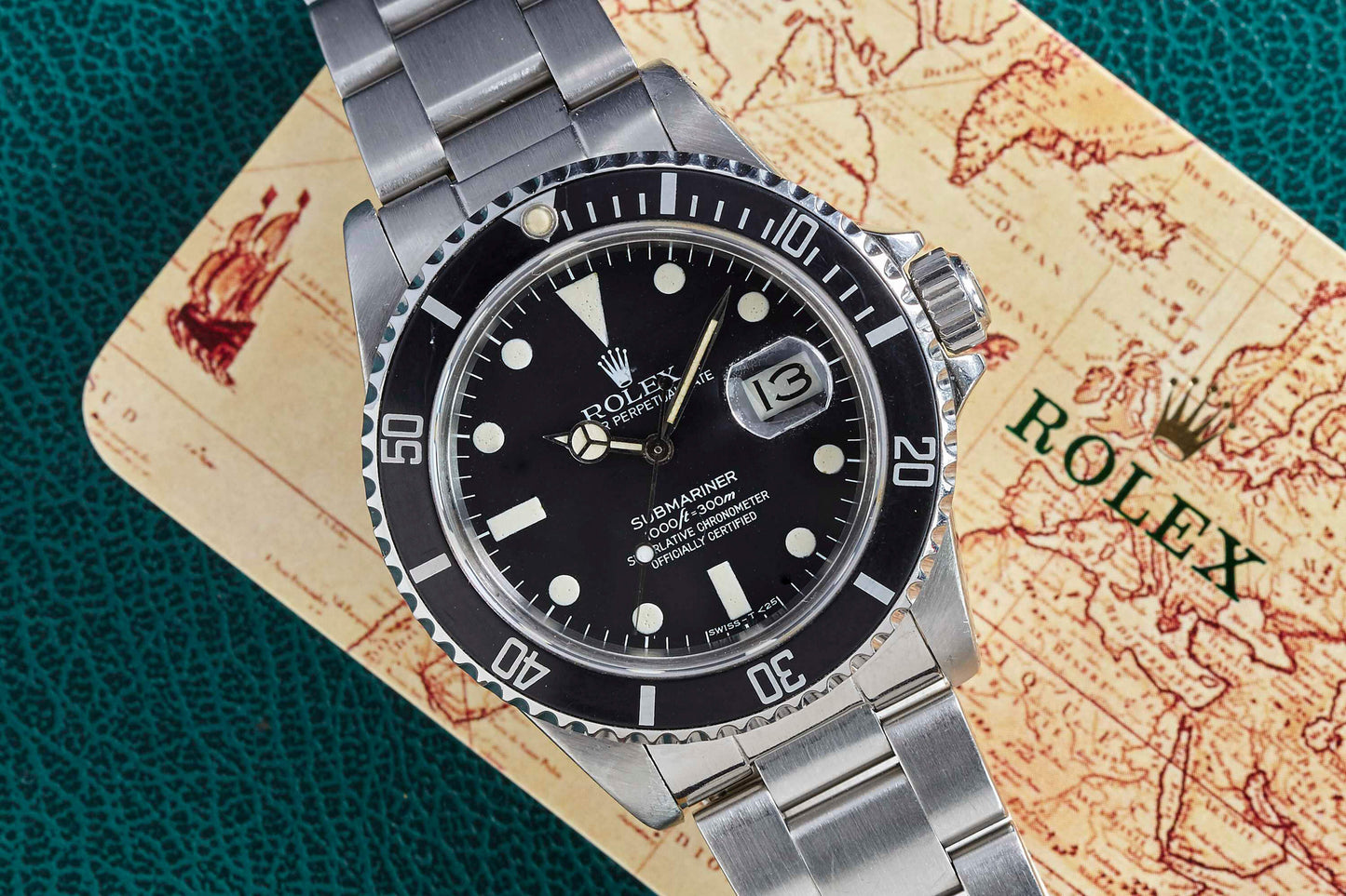 A Rolex Submariner Date by Rolex with a stainless steel band sits on a vintage map card featuring the brand logo and ship art. The black dial shows white markers and a date window.