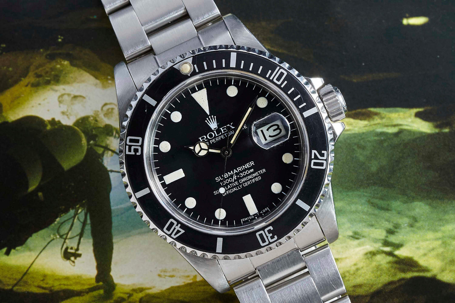 A close-up of the Rolex Submariner Date by Rolex, featuring a black dial and bezel, silver markers, stainless steel band, and date display set against an underwater diving backdrop.