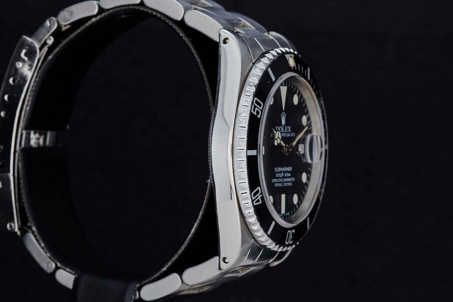 A close-up side view of the Rolex Submariner Date by Rolex, featuring a stainless steel case, black bezel, and black dial set against a plain black background. The watch's sporty yet elegant design is clearly displayed.