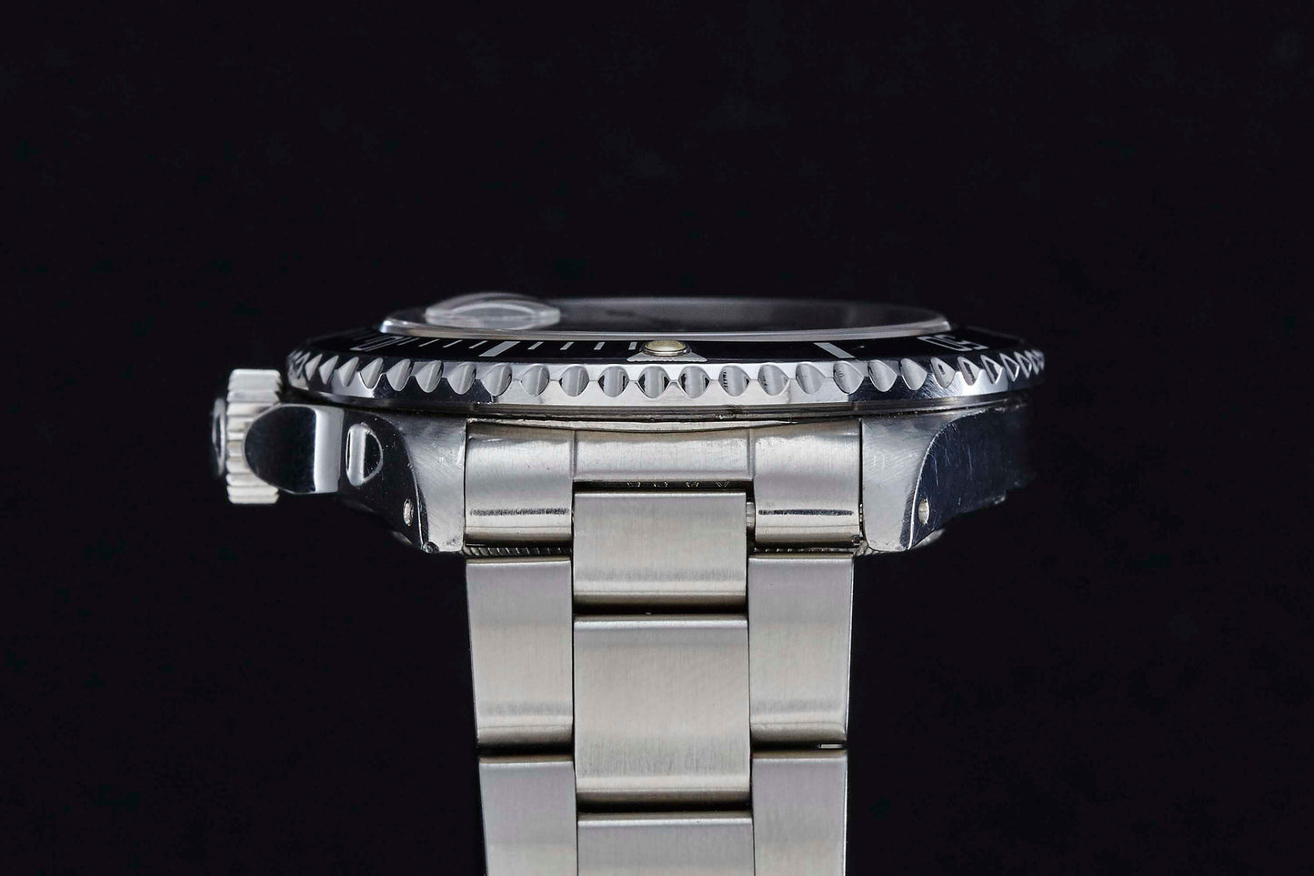 A close-up side view of a stainless steel Rolex Submariner Date by Rolex, featuring a metal bracelet, ridged bezel, and crown, set against a solid black background.