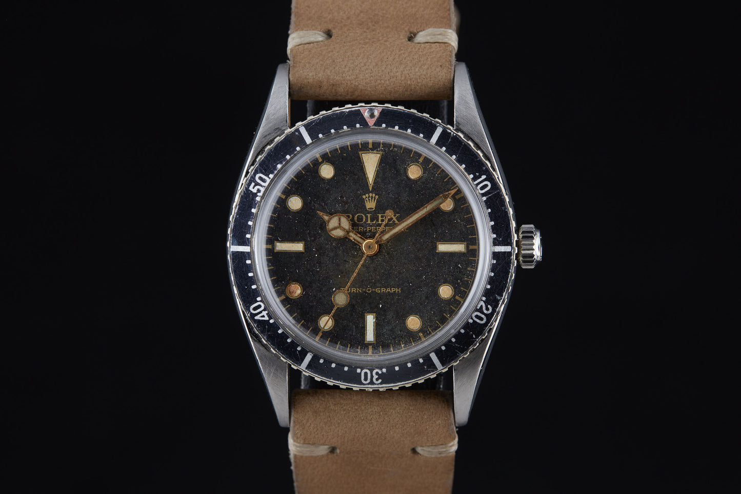 The Rolex Turn-O-Graph by Rolex is a vintage-inspired wristwatch with a black dial, round hour markers, minute-marked rotating bezel, and tan leather strap, elegantly showcased against a black background.