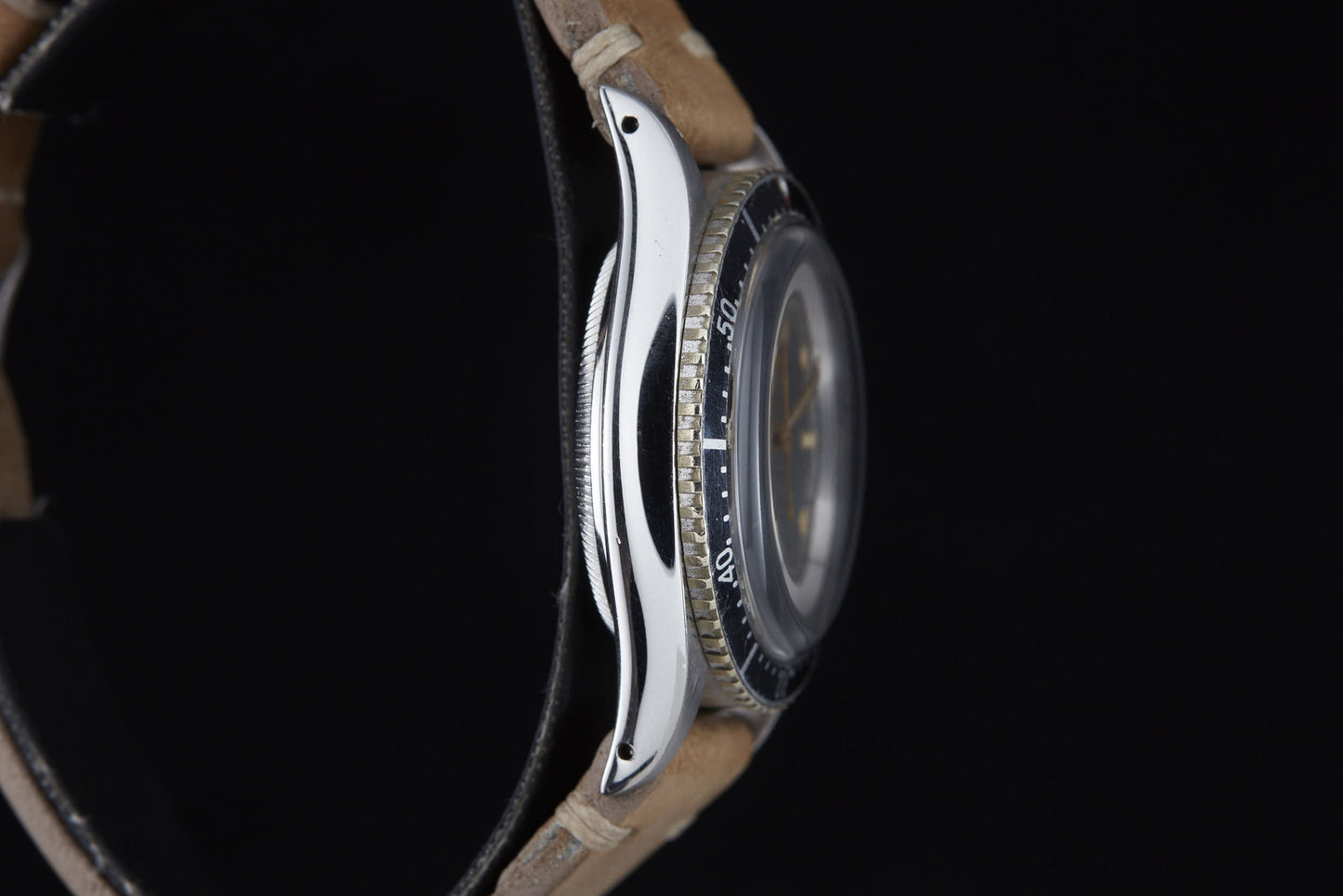 A close-up side view of the Rolex Turn-O-Graph by Rolex, featuring a brown leather strap, silver case, and rotating bezel against a black background, with the watch face obscured from this angle.