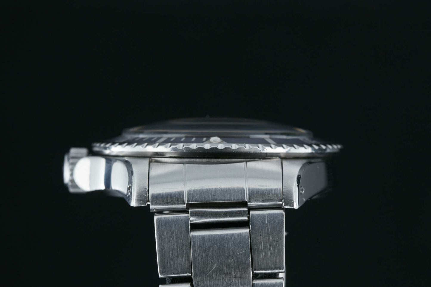 Close-up side view of the Tudor Submariner Snowflake by Tudor, showcasing its silver metal case, bezel, and part of the bracelet against a black background. Detailed description coming soon!.
