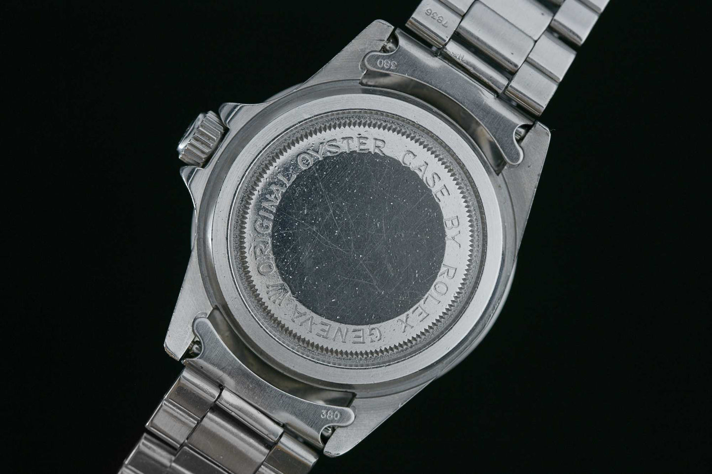 Close-up of the back of a stainless steel Tudor Submariner Snowflake wristwatch with visible scratches. Text engraved around the case references its origins. The watchband is also stainless steel. Detailed Description Coming Soon!.