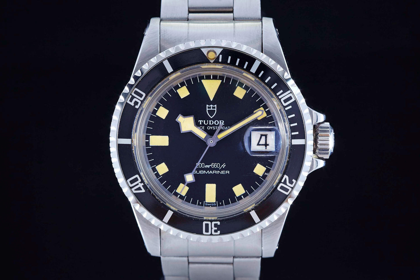 A close-up of the Tudor Snowflake Submariner by Tudor, featuring a black dial, yellow hour markers, date window at 3 o’clock, and stainless steel bracelet with an iconic Oyster case, set against a black background.