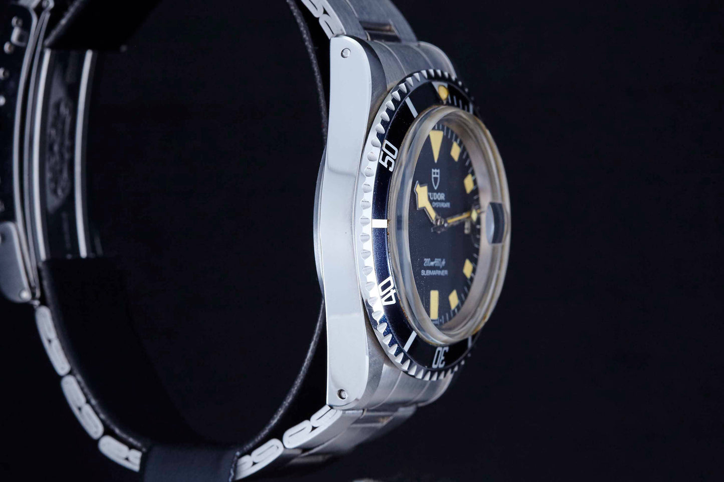 A close-up side view of the Tudor Snowflake Submariner by Tudor, featuring a black bezel, luminous hour markers, silver case, and metal bracelet against a black background.