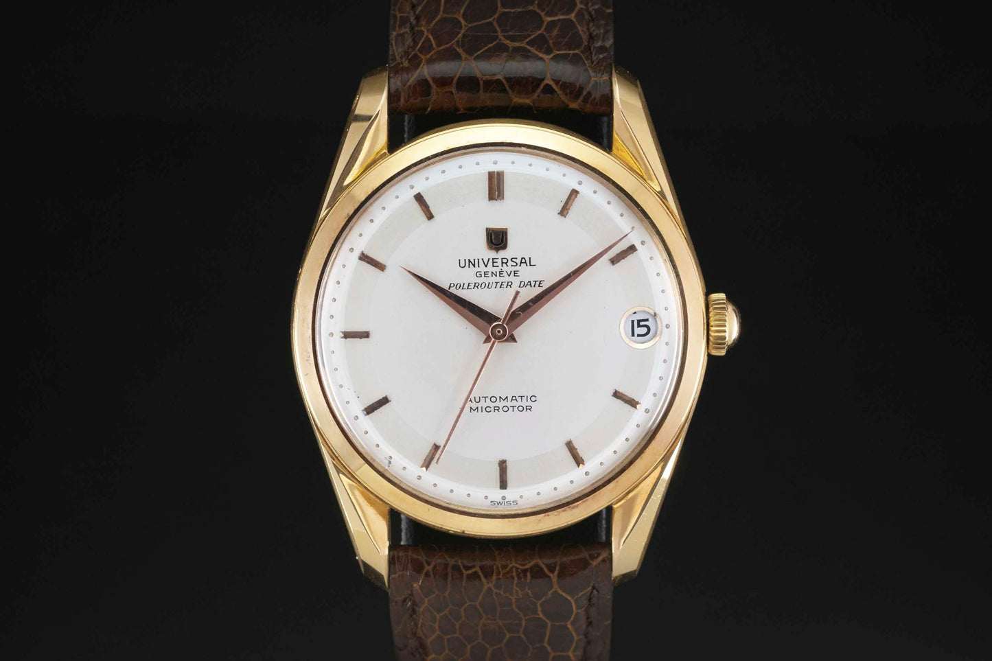 The Universal Genève Polerouter Date is a gold dress watch with a white dial, simple hour markers, elegant gold hands, date window at 3 o’clock, and a brown leather strap—perfect for sophisticated occasions.