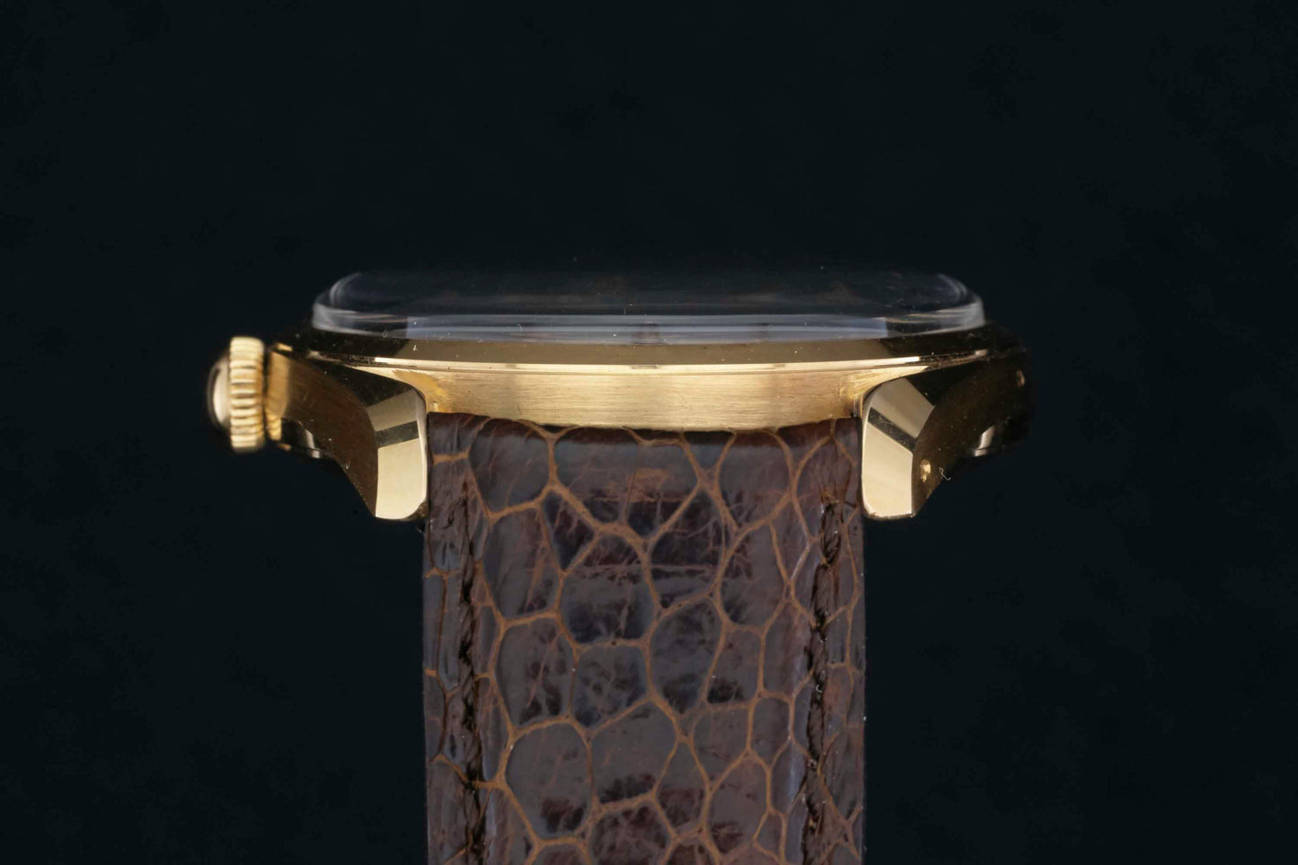 Side view of a Universal Genève Polerouter Date gold case by Universal Geneve with a brown textured leather strap, set against a black background. The crown and lugs evoke vintage elegance; the watch face remains unseen.