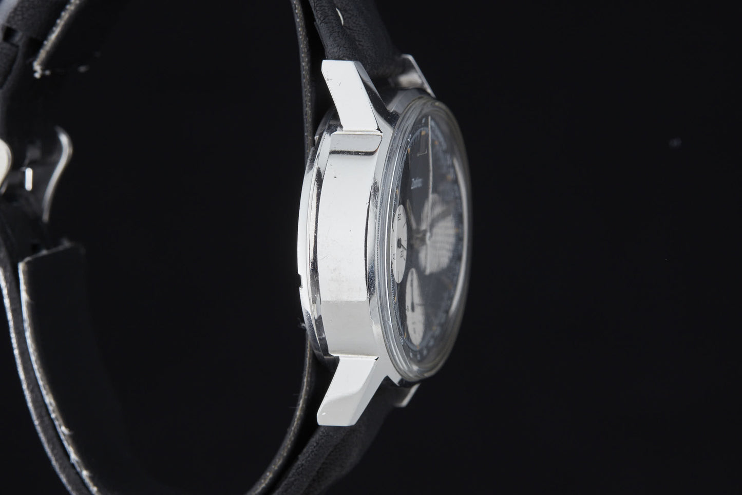 A close-up side view of the Zodiac Triple Register Chronograph shows its shiny silver case and black leather strap, set against a black background. The partially visible dial hints at the watch's intricate movements.