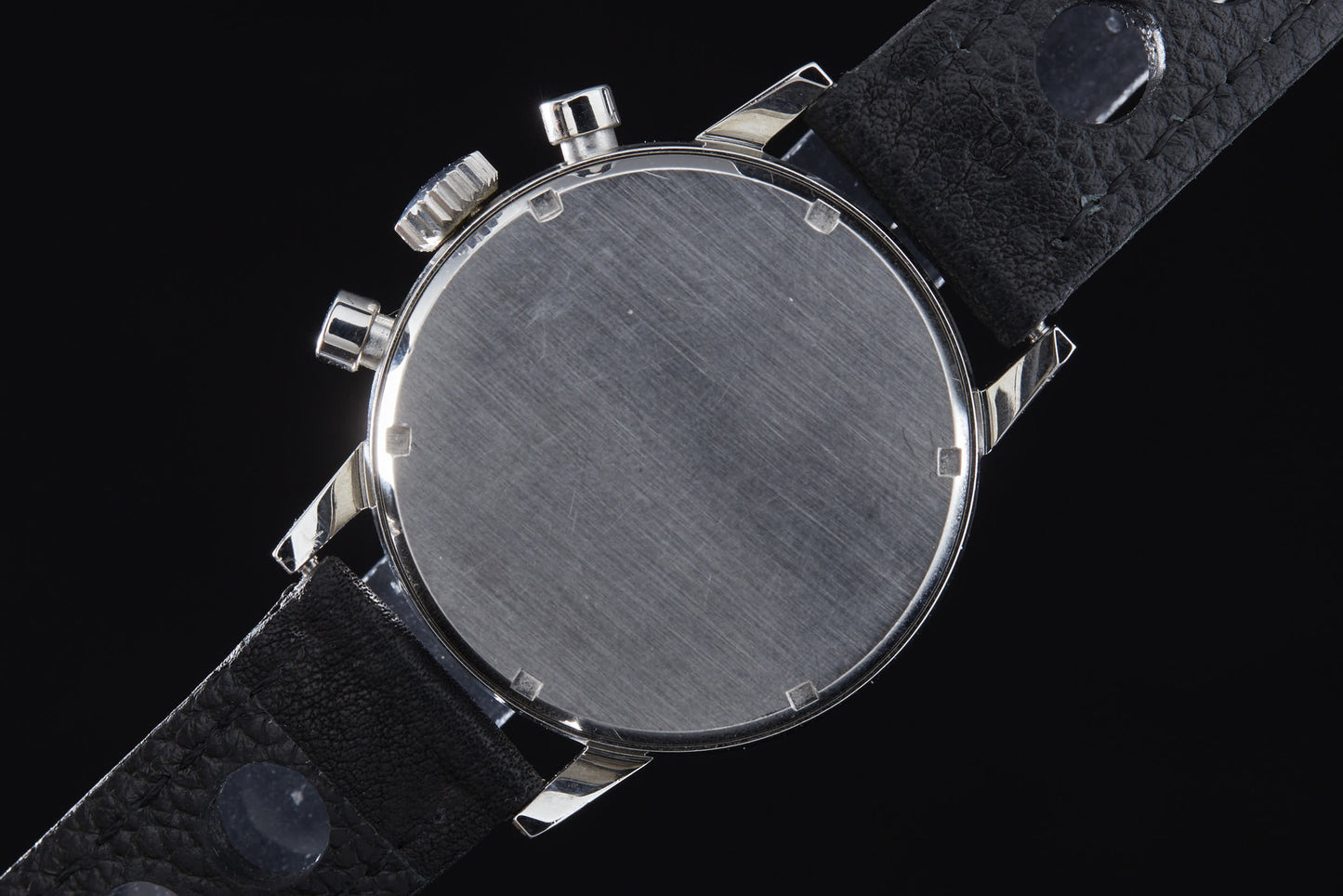 A close-up of the Zodiac Triple Register Chronograph by Zodiac shows its vintage brushed silver case back and black leather strap, with no visible branding or markings, set against a black background.