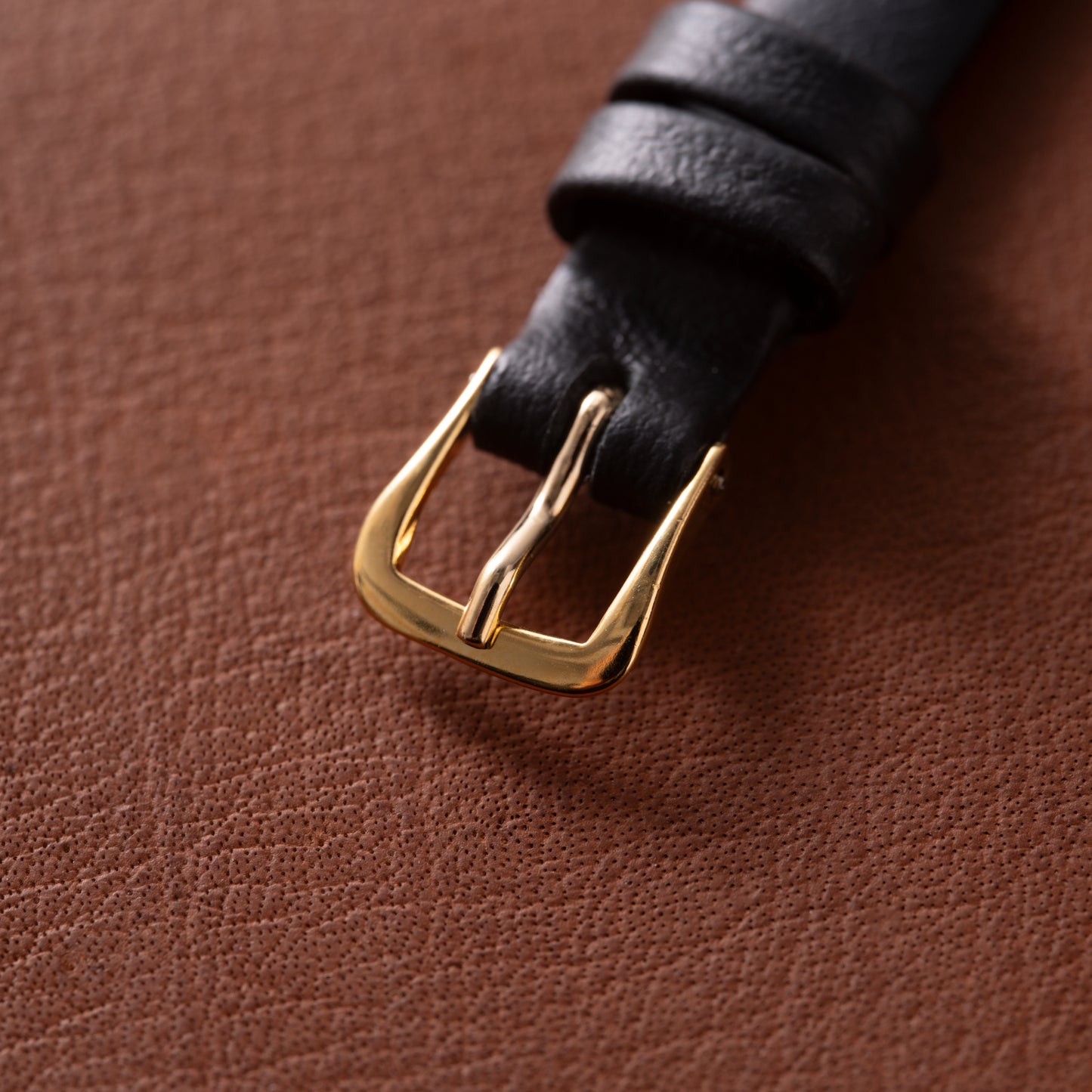 A close-up of a black leather strap with an 18K yellow gold buckle from the Patek Philippe Calatrava 'Tiffany & Co' ladies watch, resting on textured brown leather.