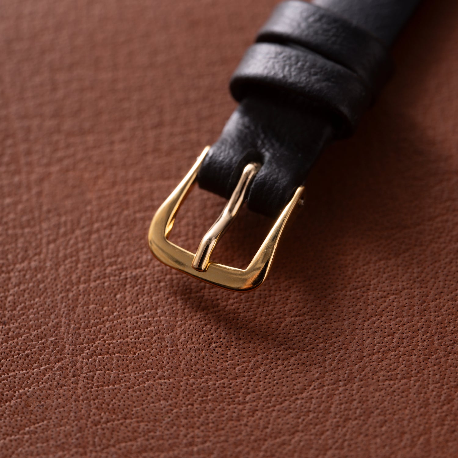 A close-up of a black leather strap with an 18K yellow gold buckle from the Patek Philippe Calatrava 'Tiffany & Co' ladies watch, resting on textured brown leather.