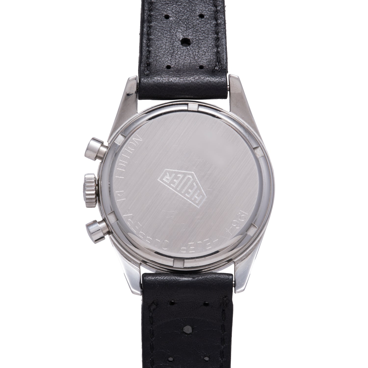 The back of the TAG Heuer 1964 Carrera Re-Edition shows a brushed metal case with engraved logo and black perforated leather strap. Two crown buttons are visible on the side of this vintage TAG Heuer chronograph.