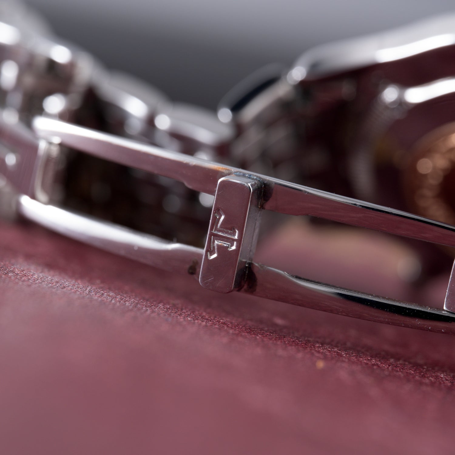 Close-up of a Jaeger-LeCoultre Master Control Chronograph Mecaquartz silver bracelet with engraved JL initials on the clasp, resting on burgundy. The shot emphasizes the shiny reflective metal links and fine craftsmanship.