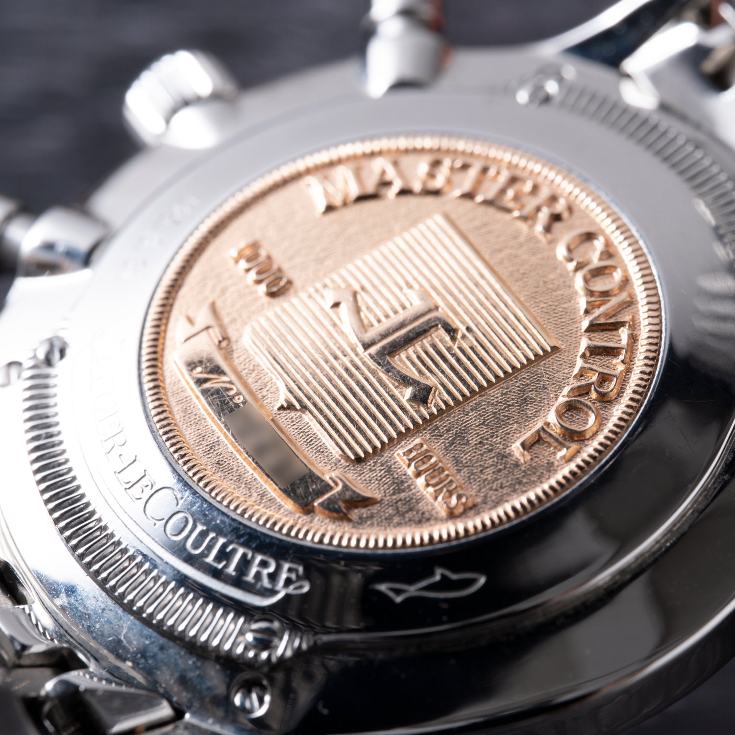 Close-up of the Jaeger-LeCoultre Master Control Chronograph Mecaquartz case back, showcasing a gold-toned medallion, intricate engravings, and emblem. The polished finish accentuates the precision of its Calibre 630 Mecaquartz movement.