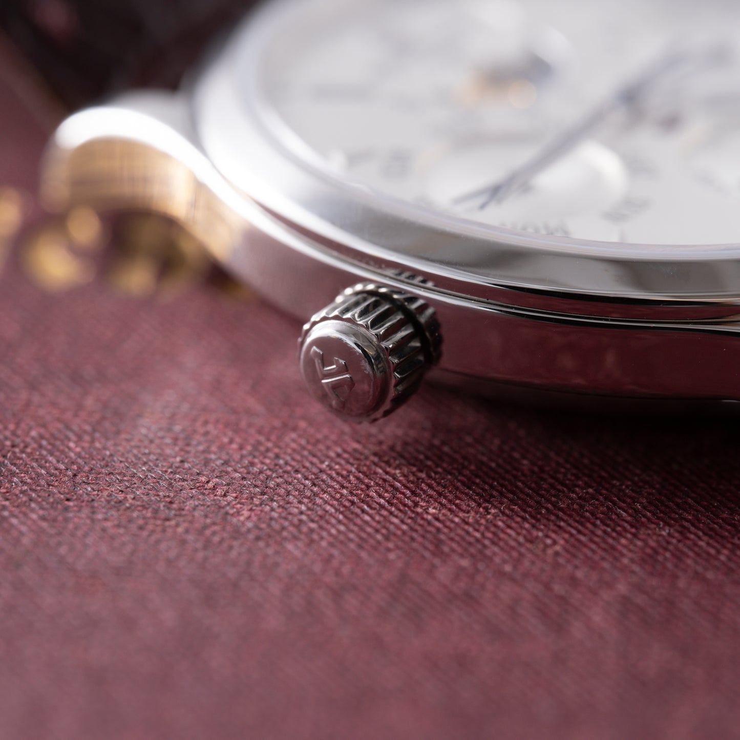 Close-up of the Jaeger-LeCoultre Master Control Perpetual Calendar crown and case, highlighting fine details as it rests on a textured burgundy surface with blurred gold lettering in the background.