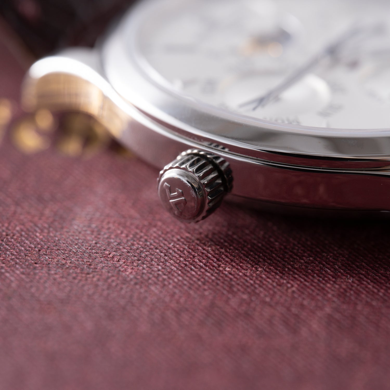 Close-up of the Jaeger-LeCoultre Master Control Perpetual Calendar crown and case, highlighting fine details as it rests on a textured burgundy surface with blurred gold lettering in the background.