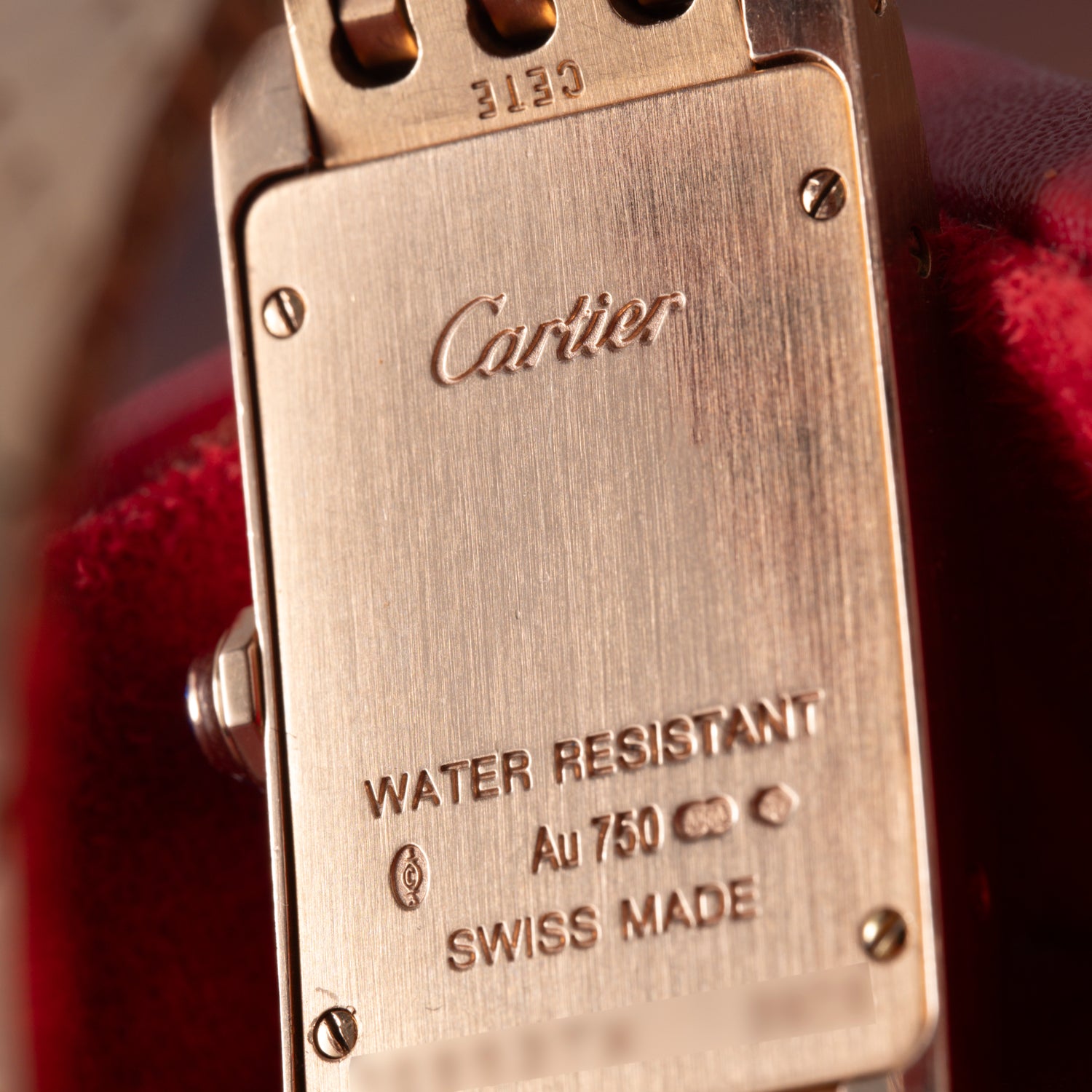 Close-up of the back of a Cartier Tank Americaine ladies watch in 18K rose gold, engraved with Cartier, WATER RESISTANT, Au 750, hallmarks, and SWISS MADE.