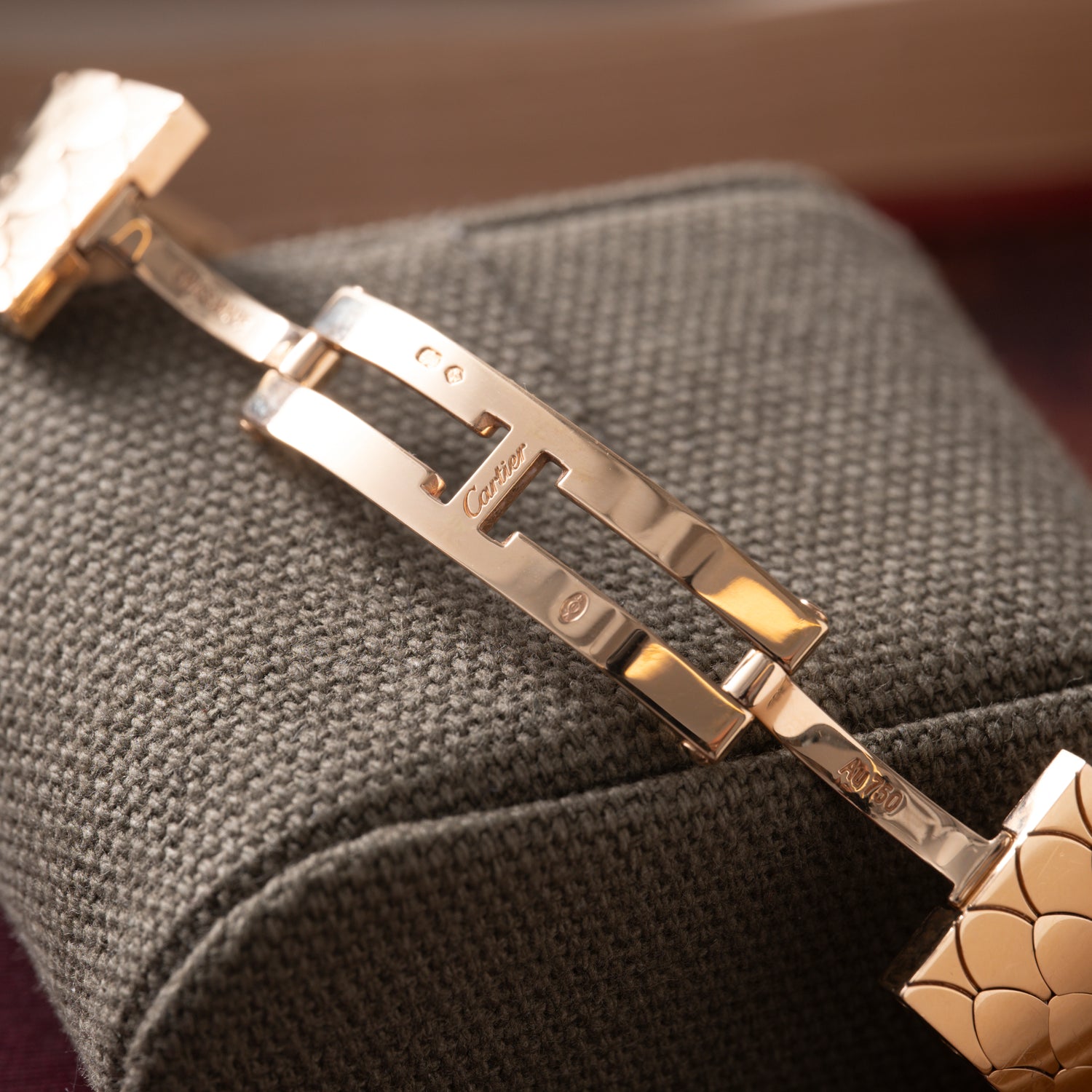 Close-up of a Cartier Tank Americaine Automatic Diamonds clasp in polished 18K rose gold, engraved with Cartier branding and visible hallmarks, displayed open on a textured dark gray fabric cushion.