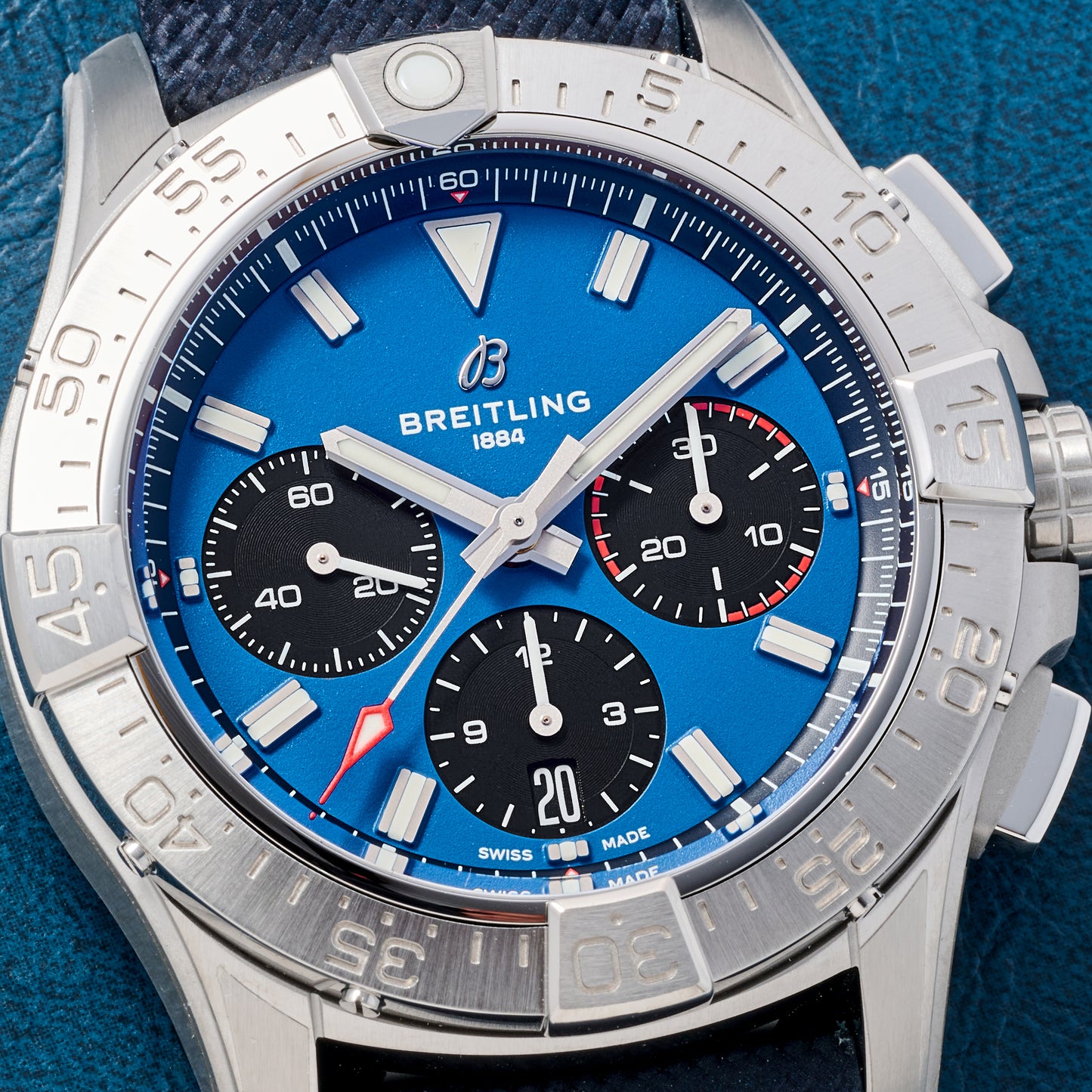 A close-up of the Breitling Avenger B01 Chronograph 42 by Breitling, showcasing a blue dial, silver bezel, three black subdials, silver hour markers and hands, all on a textured dark strap.