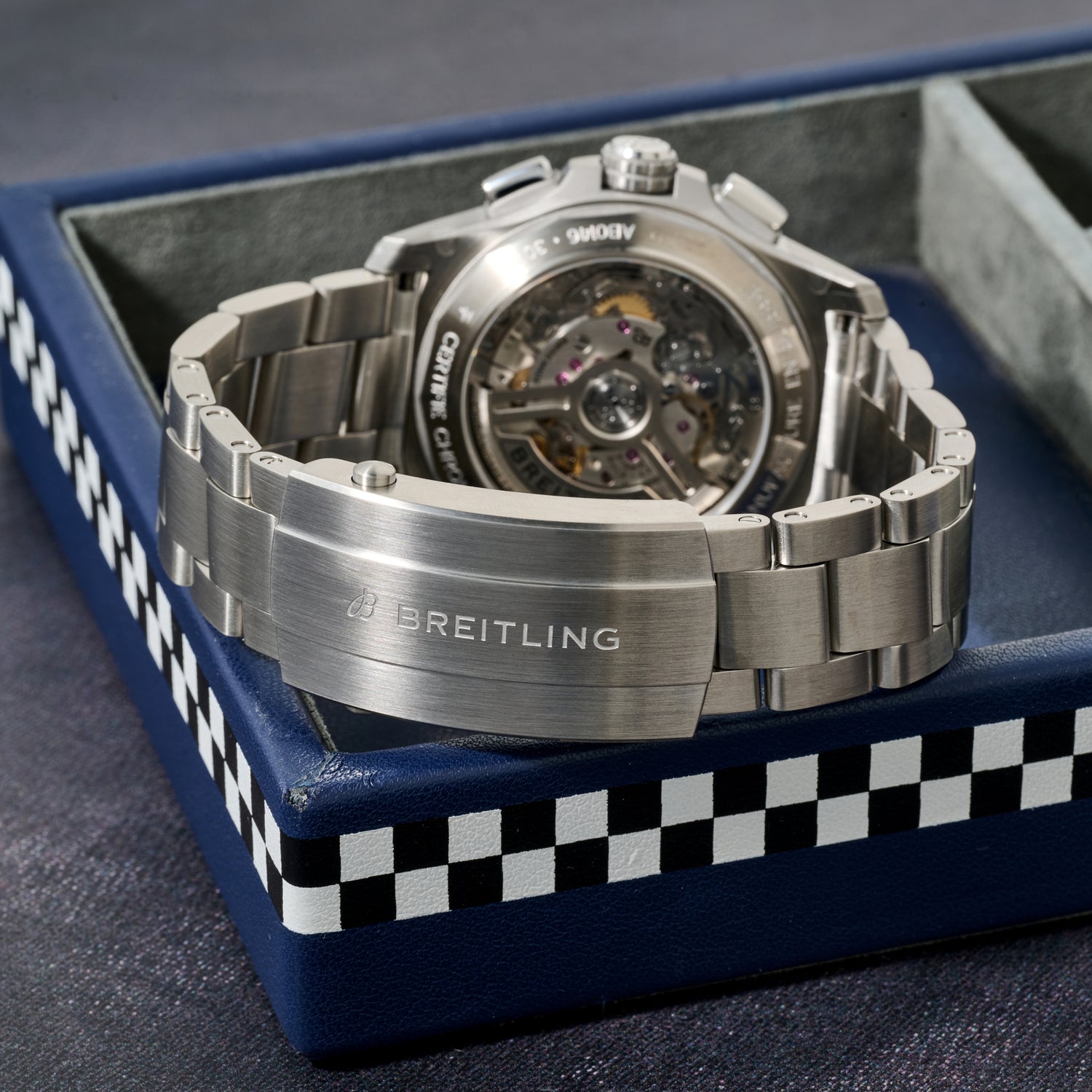 A silver Breitling Avenger B01 Chronograph 42 watch with a visible COSC-certified automatic movement is displayed on a blue Breitling box with black and white checkerboard edging.