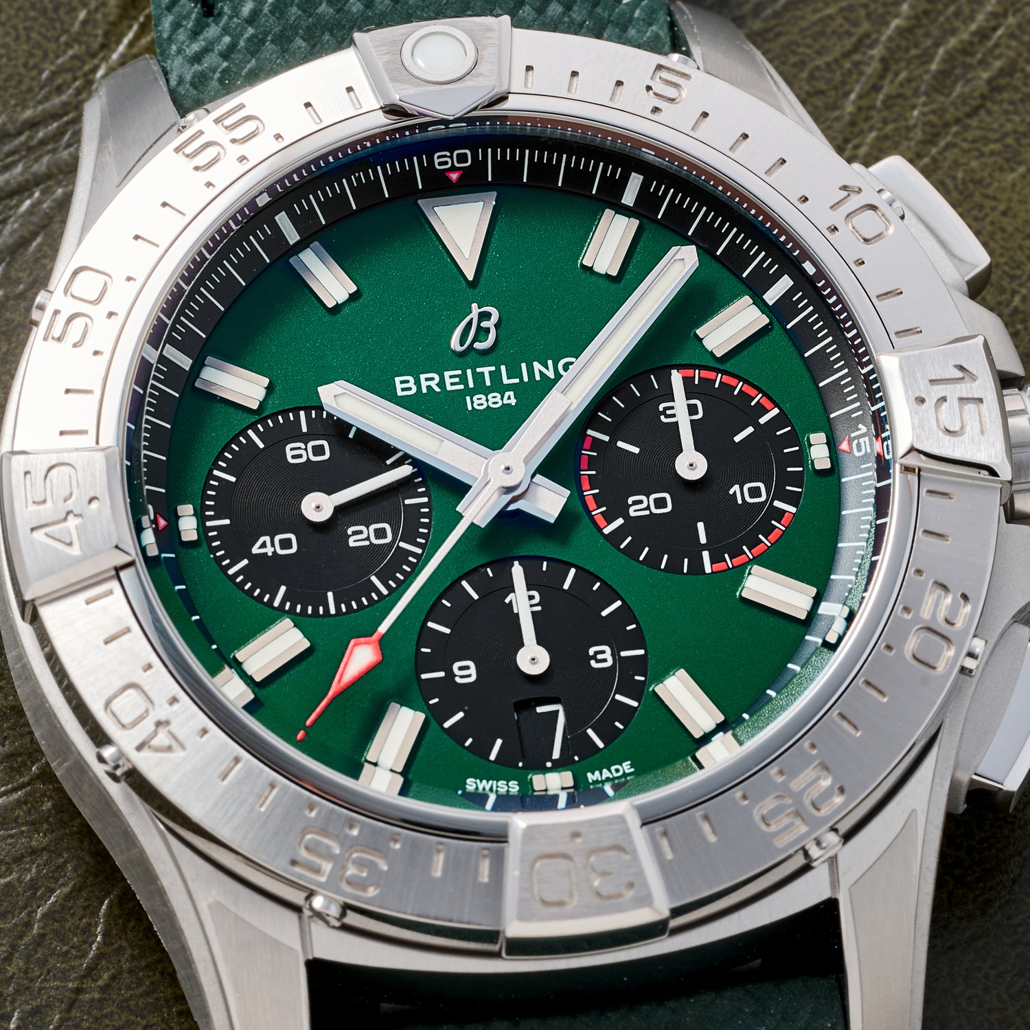 A close-up of the Breitling Avenger B01 Chronograph 42 by Breitling, featuring a green dial, silver bezel, three subdials, a date window at 6 o’clock, and shown on a textured green strap.