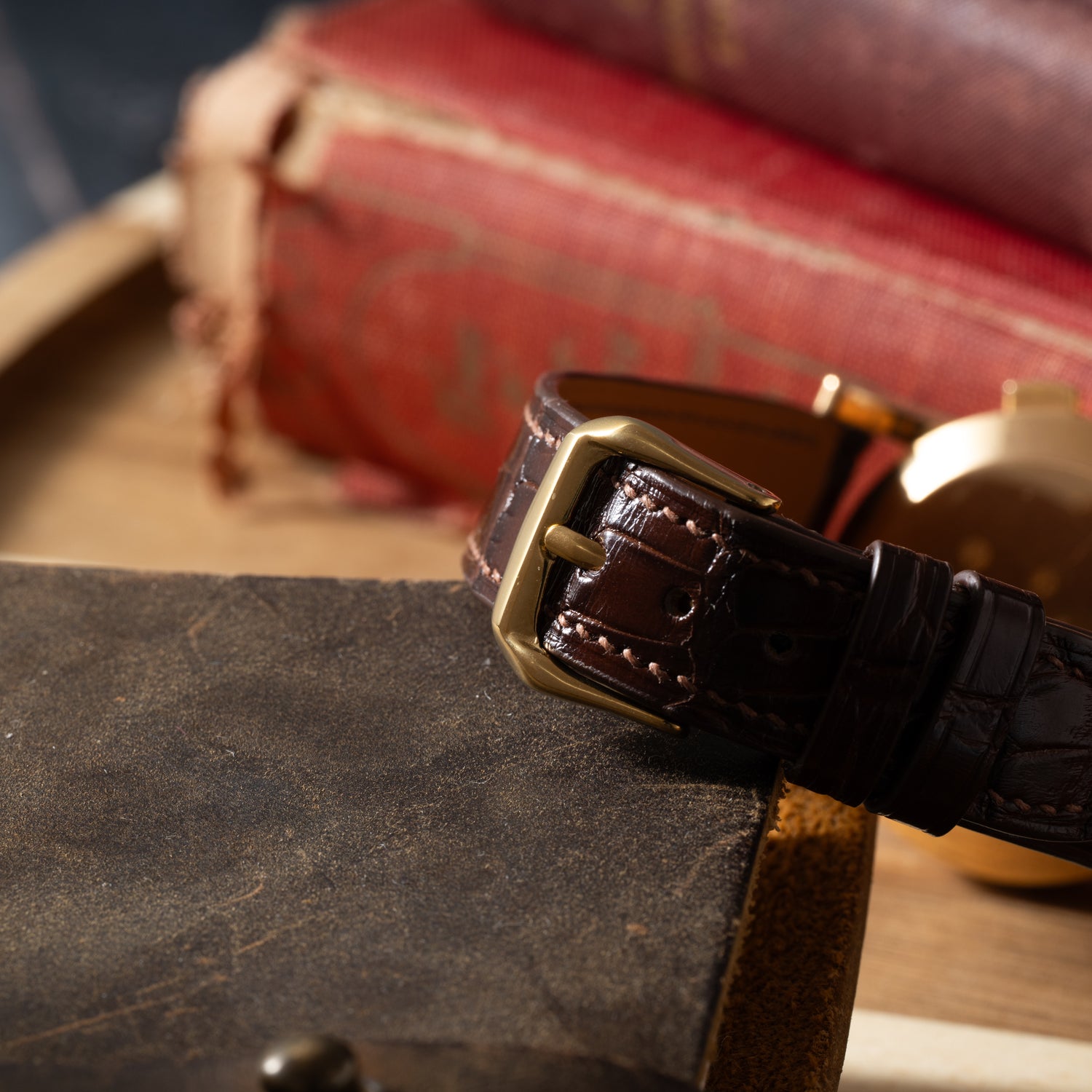 A close-up of a brown leather watch strap with a brass buckle from the Omega French Market Chronograph 'Calibre 321', resting on an old, worn book, with blurred stacks of books in the background.