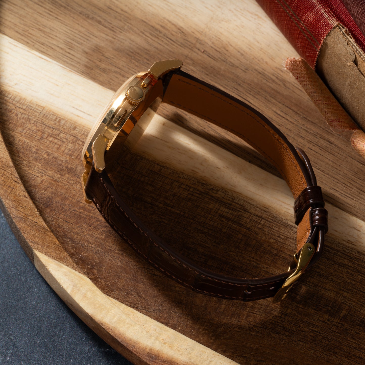 An Omega French Market Chronograph 'Calibre 321' gold wristwatch with a brown leather strap sits on a round wooden surface by a stack of books, its classic chronograph design evoking the iconic heritage of Omega.