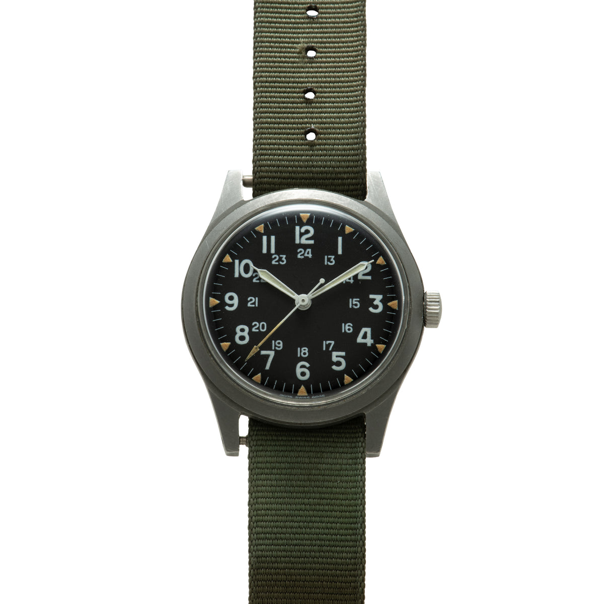 Hamilton GG-W-113 watch with black dial, 24-hour numerals, gold triangle markers, and olive green fabric strap.