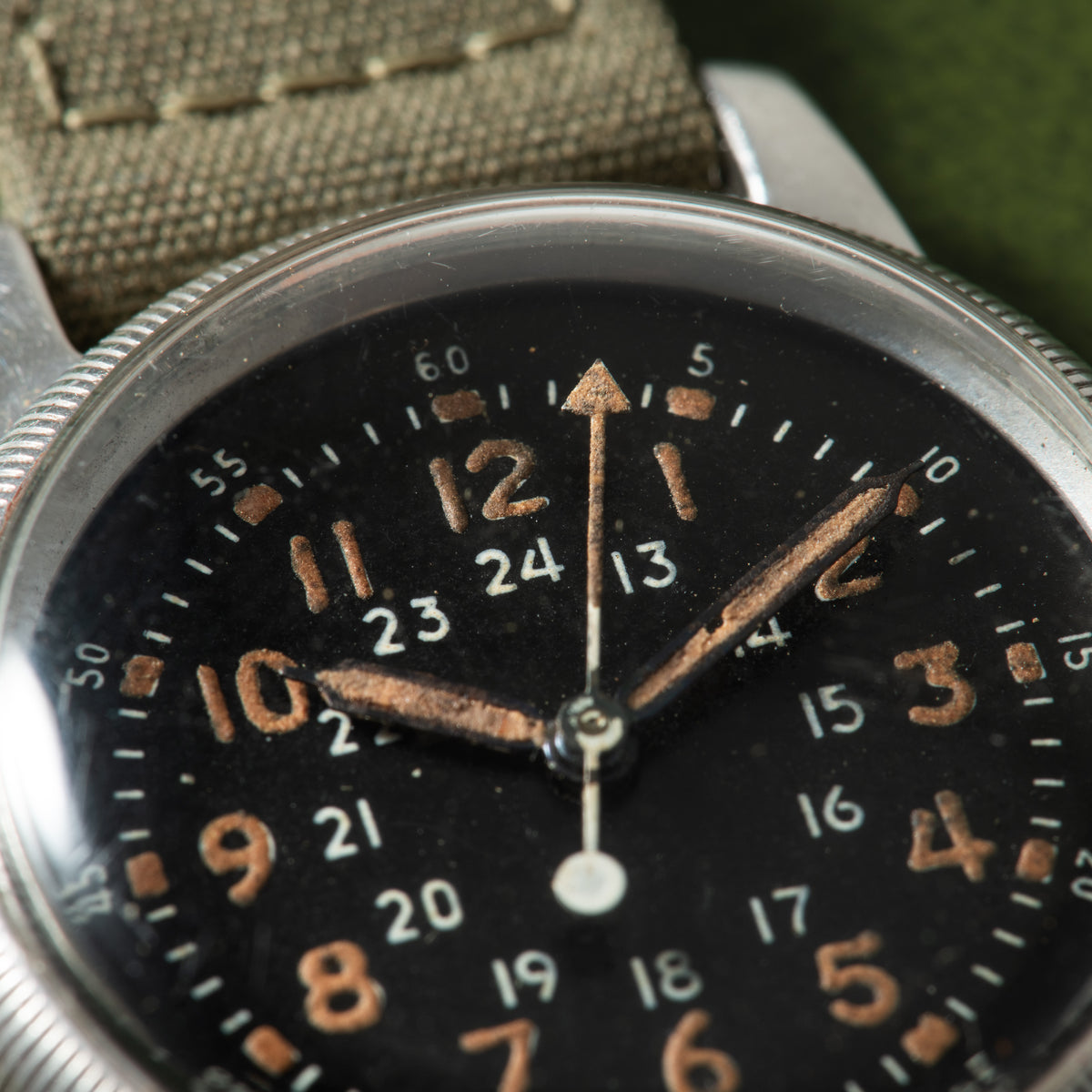 Waltham A-17 watch with black dial, copper-colored numerals and hands, showing 10:10 time, on tan fabric strap.