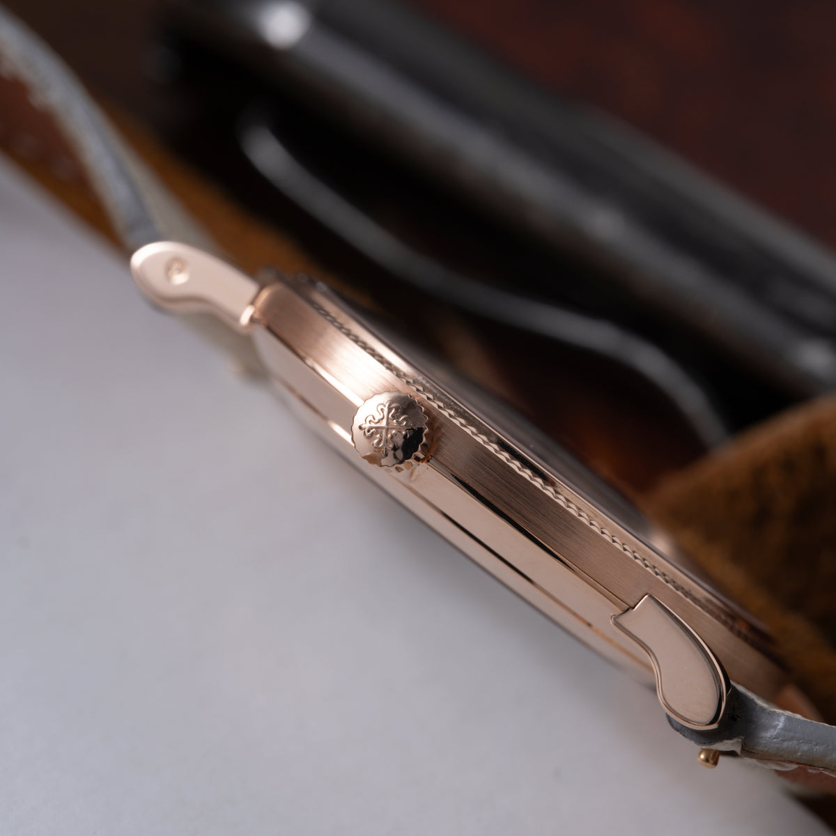 Rose gold dress watch with round case, decorative crown, and dark leather strap shown at angle.