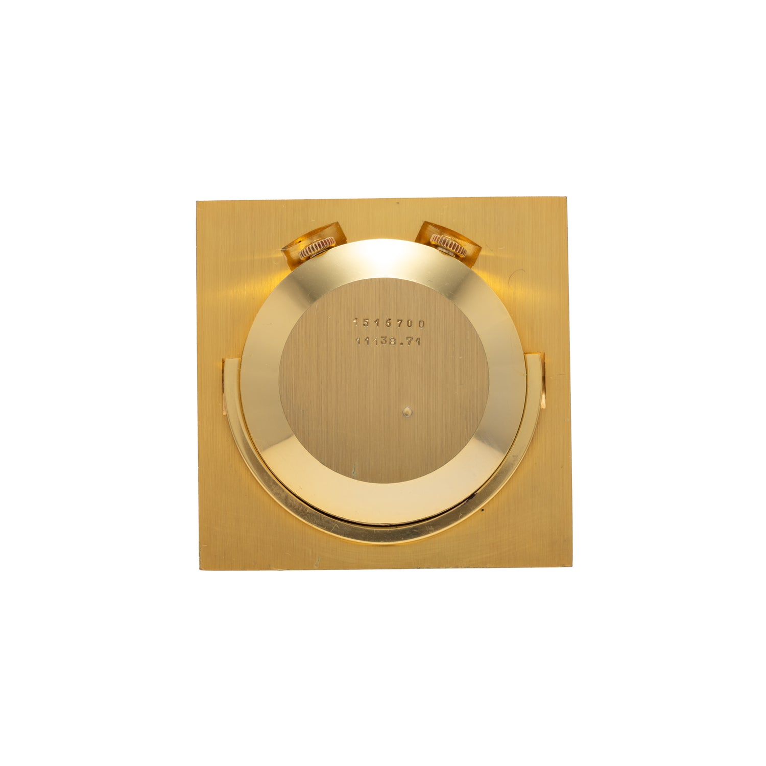 The Jaeger-LeCoultre Memovox Travel Calendar Alarm Clock features a minimalist geometric gilt-brass design with a square gold-toned case, circular center, two raised top sections, and engraved numerals and letters that highlight its craftsmanship.