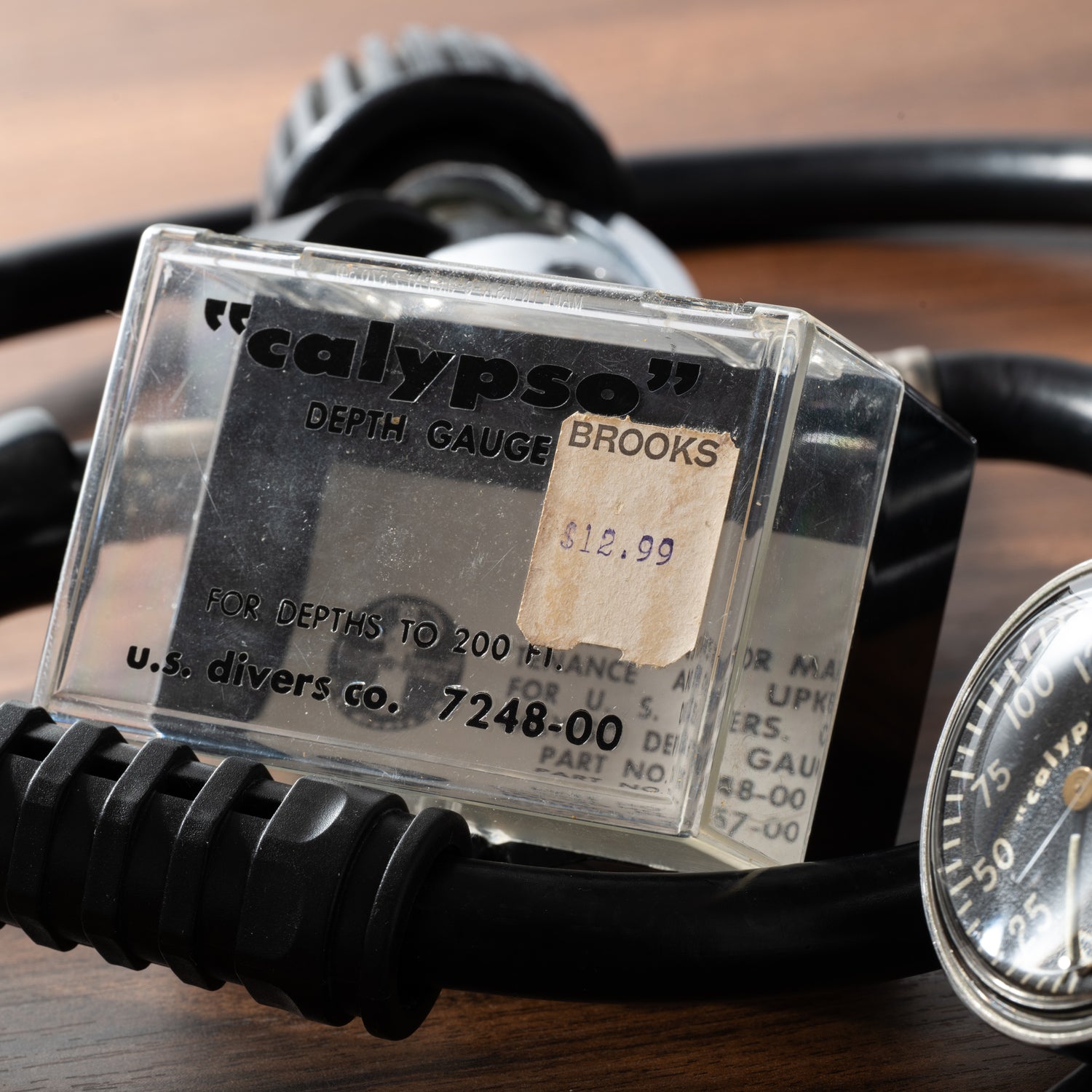 A vintage Calypso Depth Gauge by Calypso, ideal for scuba diving, is priced at $12.99 and displayed on a wood surface with black hoses and a partially visible pressure gauge in the background.